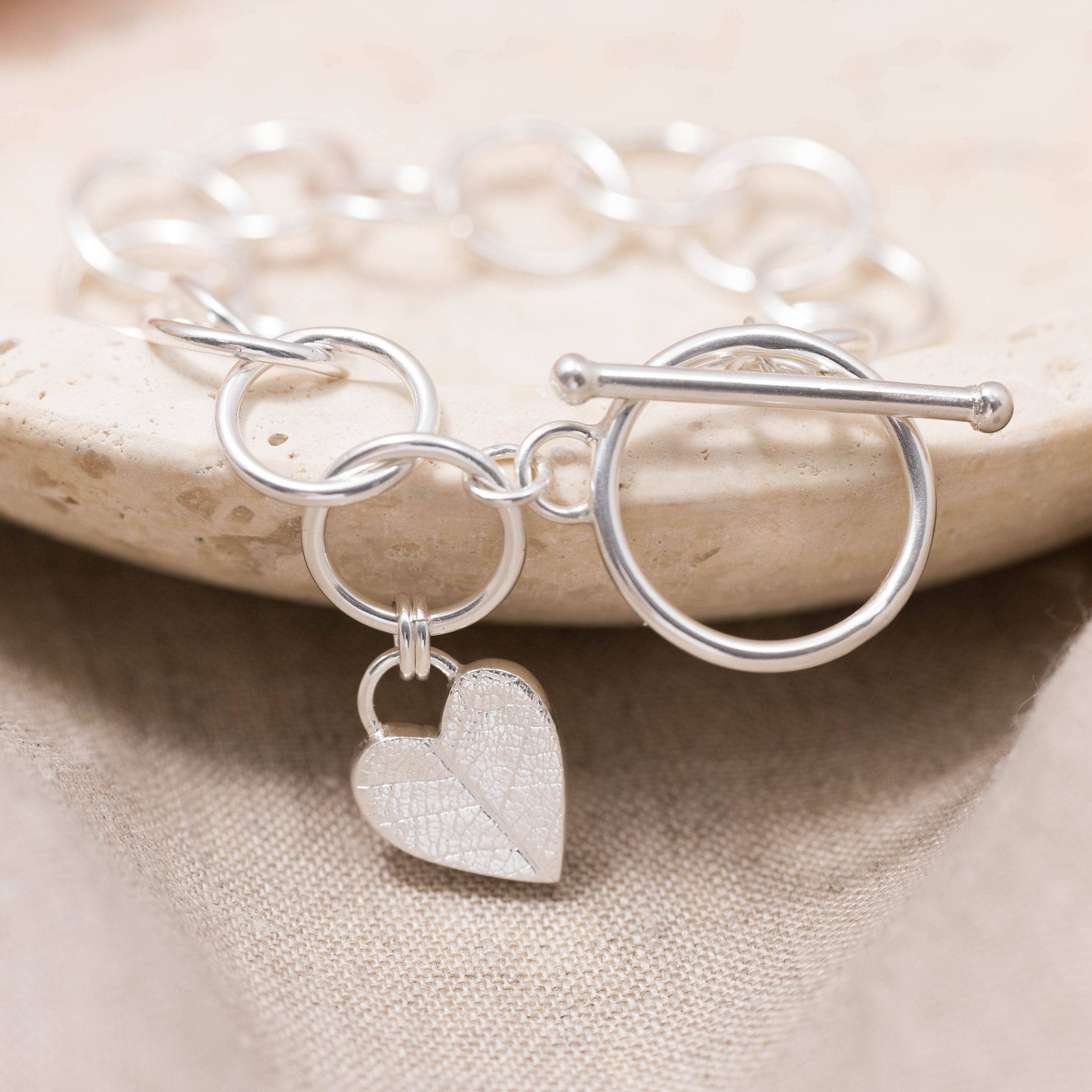 Sterling silver bracelet with a textured heart charm featuring a delicate leaf pattern, finished with a toggle clasp.