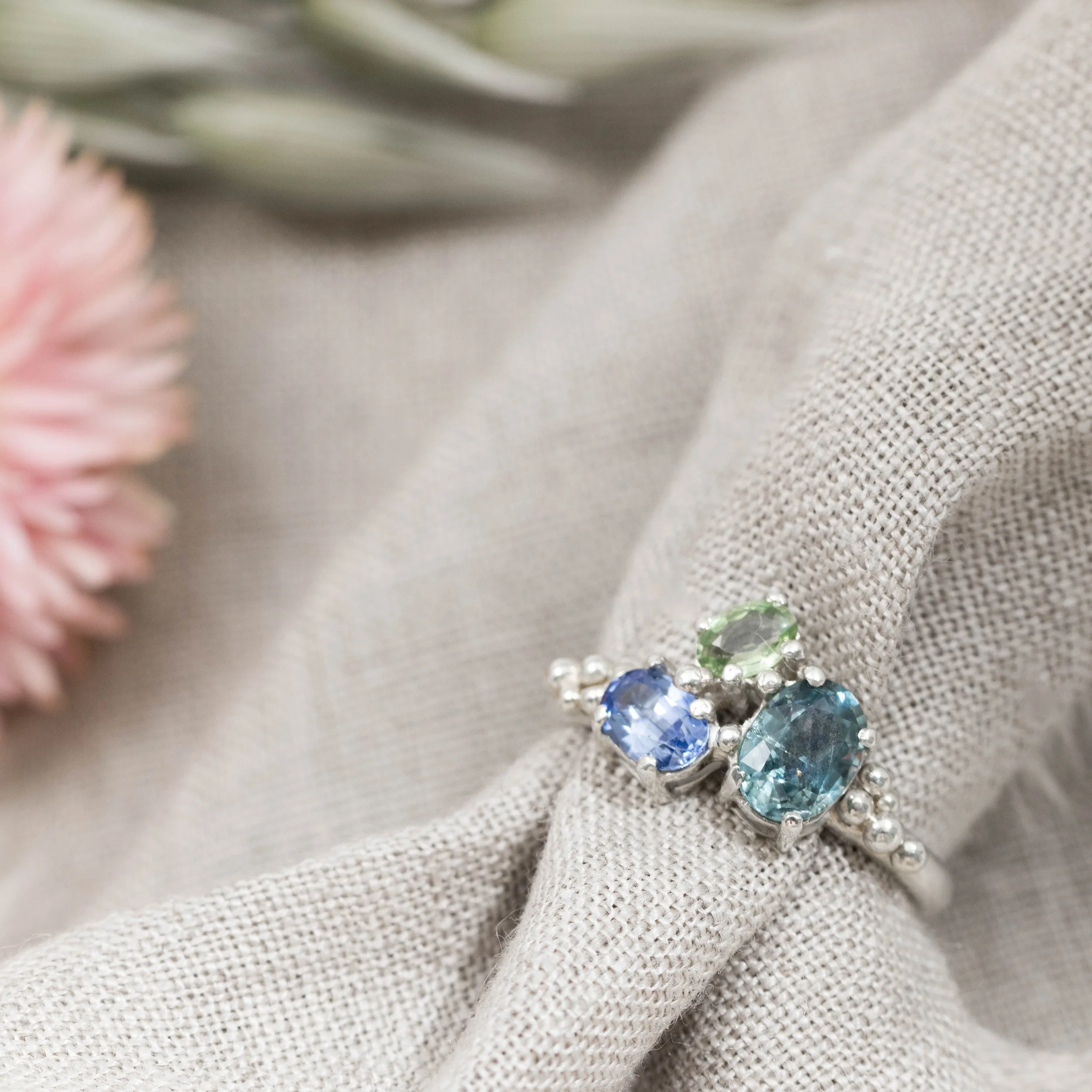 White gold ring with a cluster of oval blue and green sapphires in a seascape-inspired design.