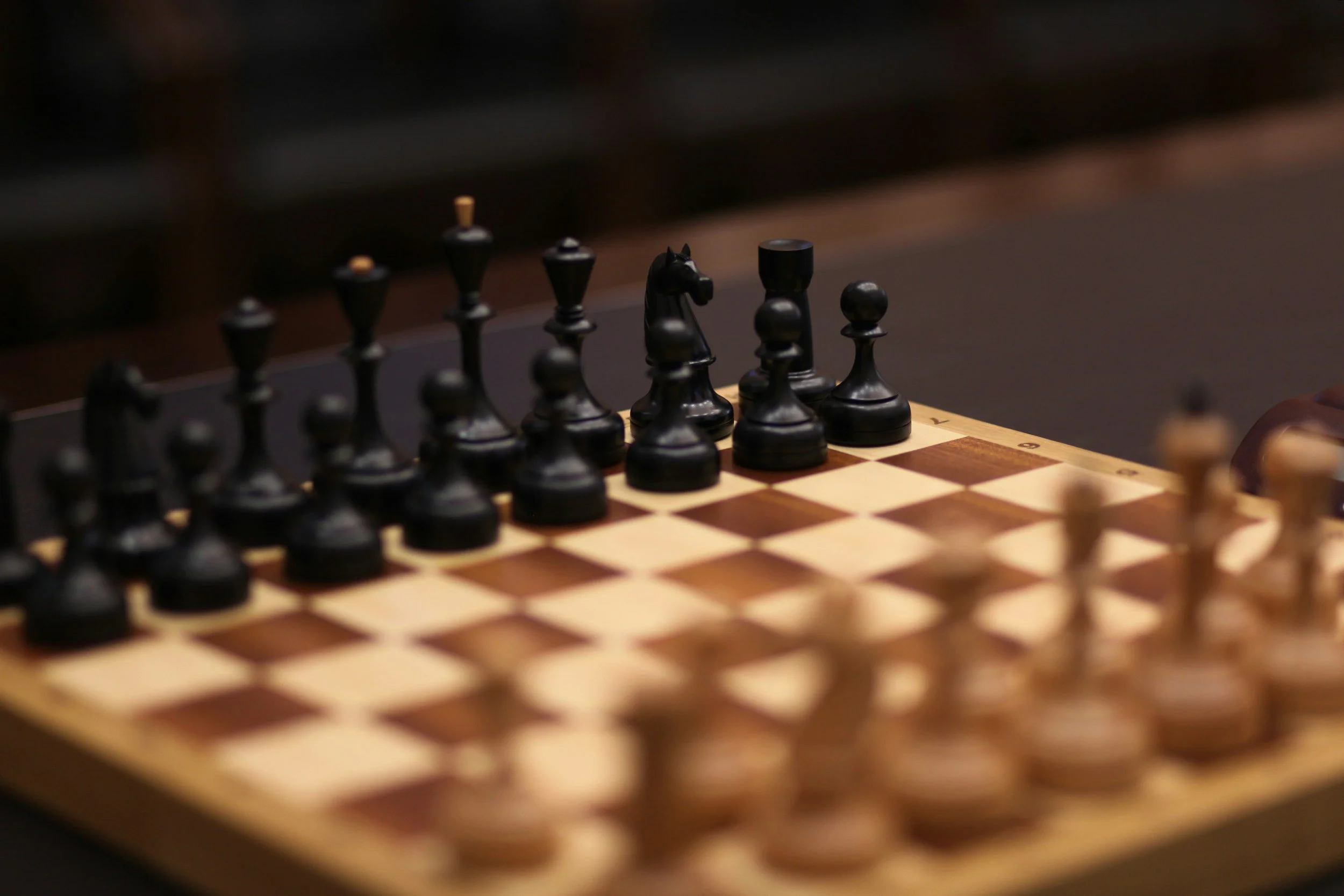 Close-up of a chessboard with black chess pieces set up for a game, focus on the black king and knight.