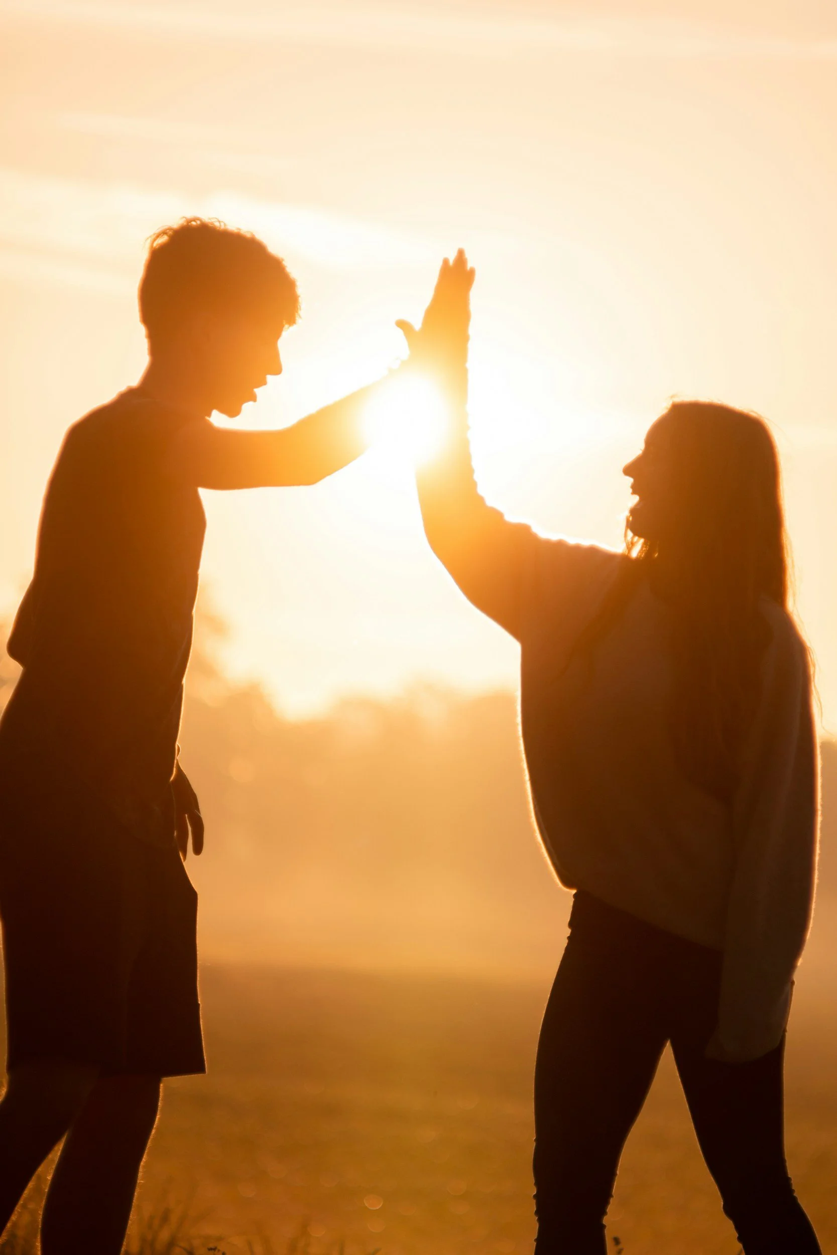 Two children giving each other a high five during sunset.