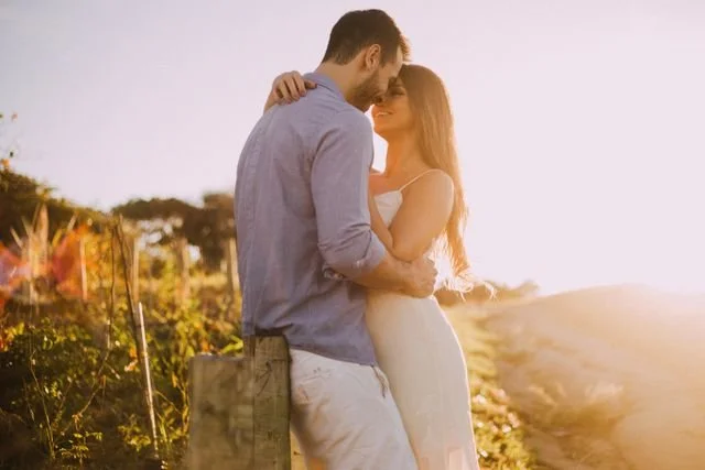 A couple hugging outside in a field by a fence