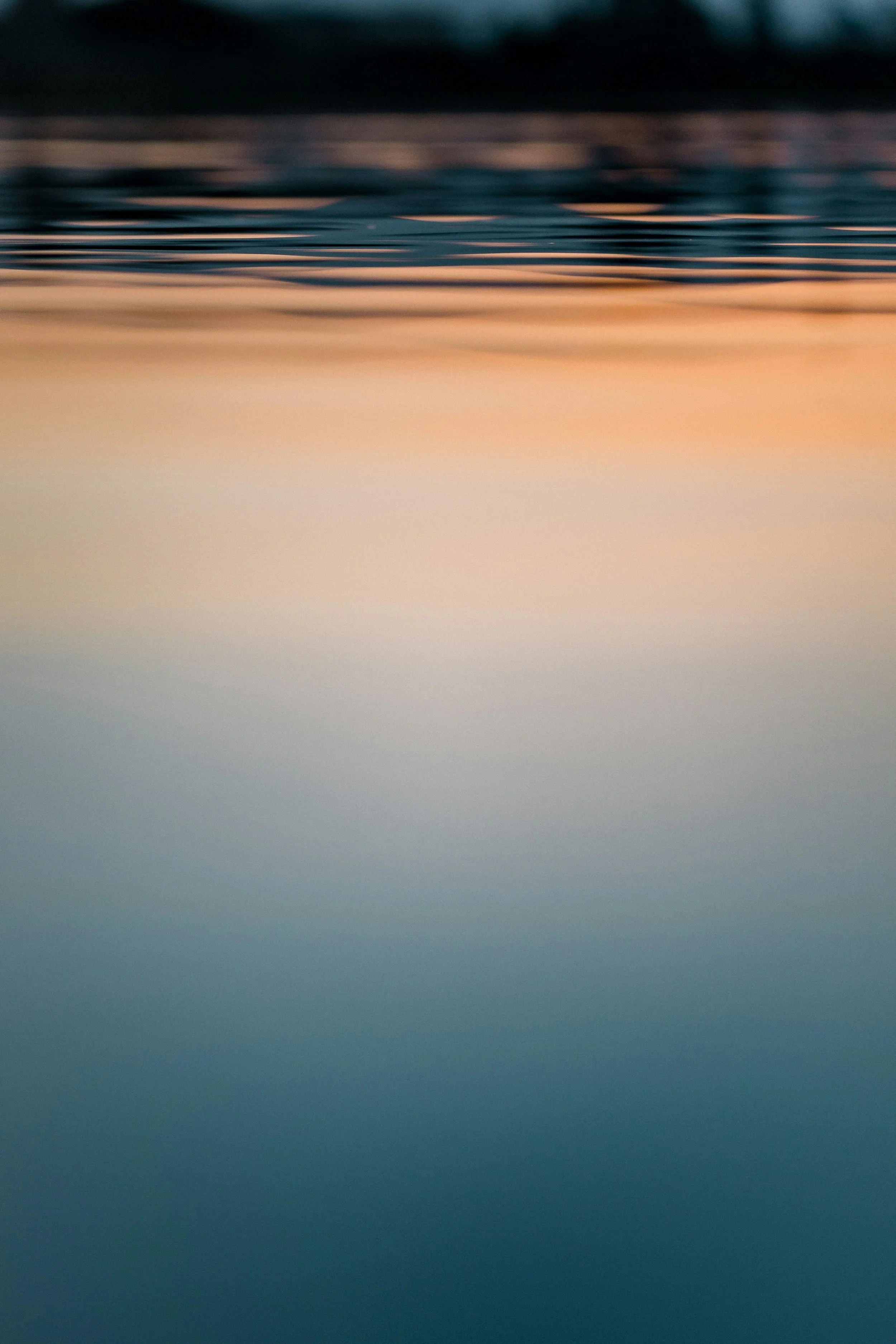 Abstract image of a calm body of water reflecting sunset colors with ripples on the surface.