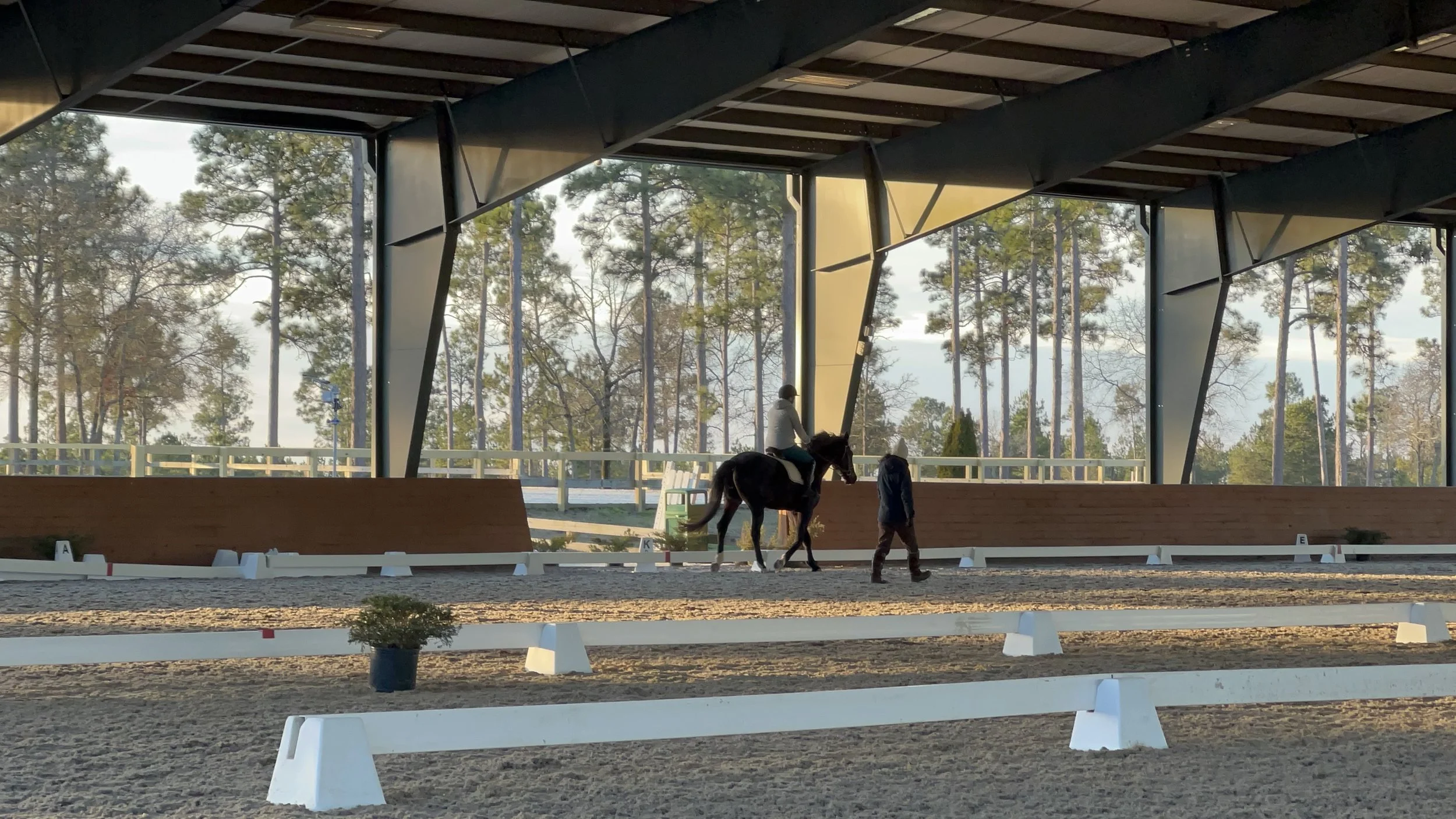 Aubrey coaching a horse and rider pair in a covered arena.