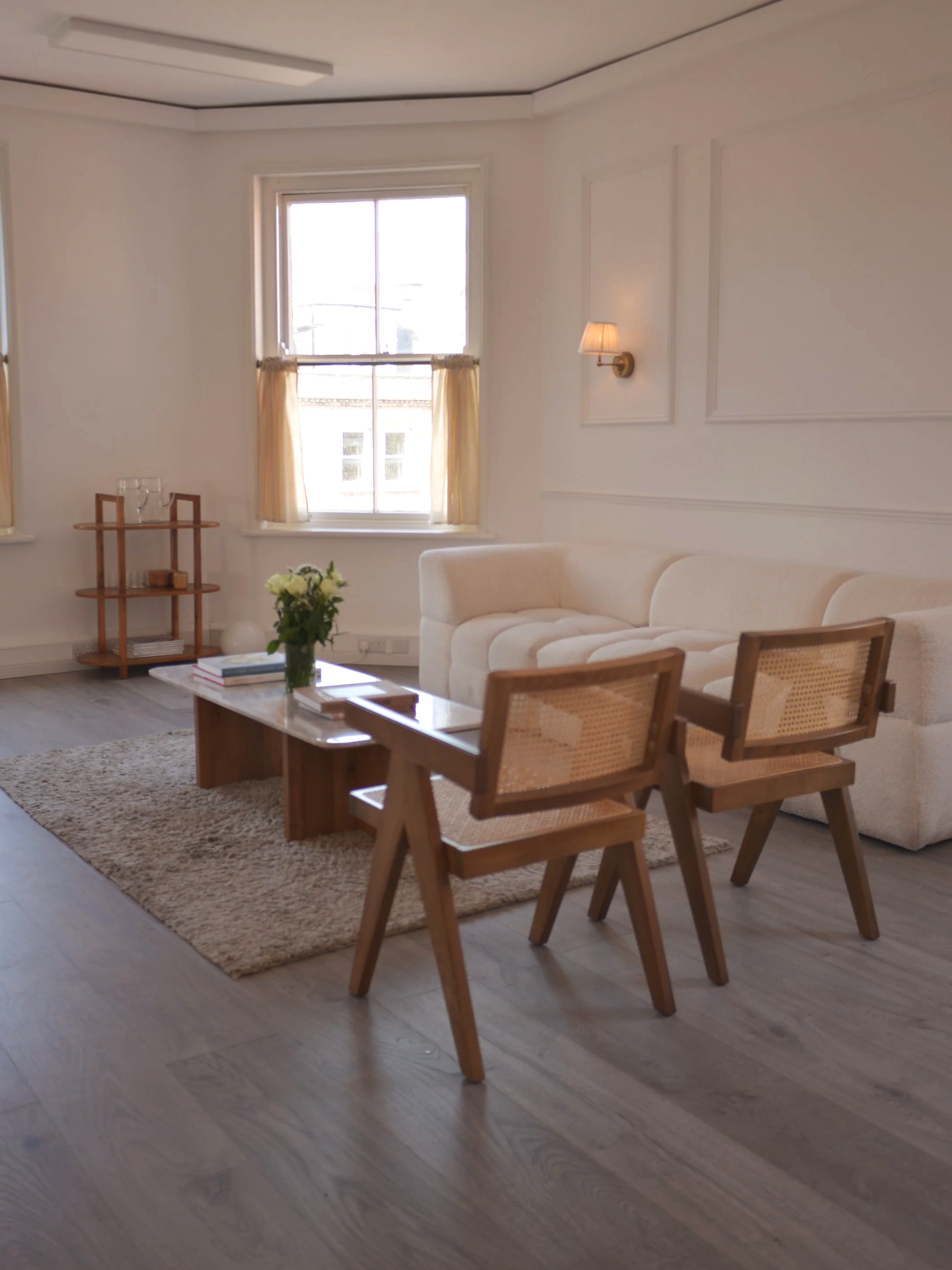 Room one - the waiting area. A beautiful light filled white room with panelled walls, our famous boucle couch, cafe curtains, linen wall lights and walnut mid century furniture
