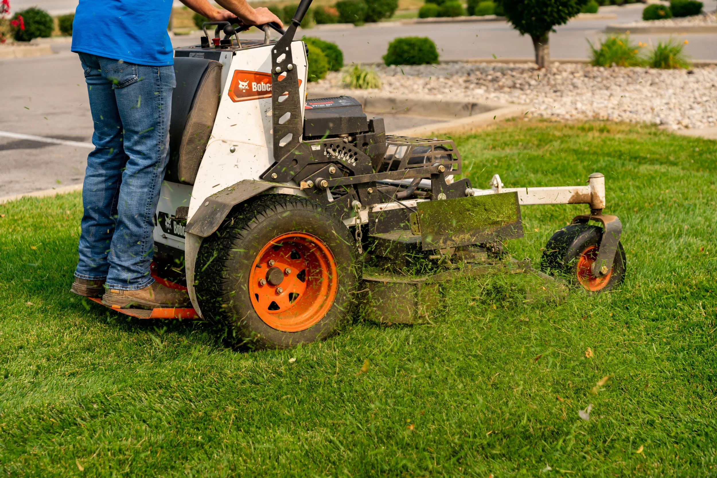 An Akers Lawn Care and Landscaping crew members mows grass, sending the cut grass flying