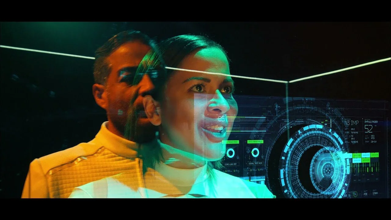 Two people, a man and a woman, in a high-tech control room with holographic displays and futuristic interfaces.