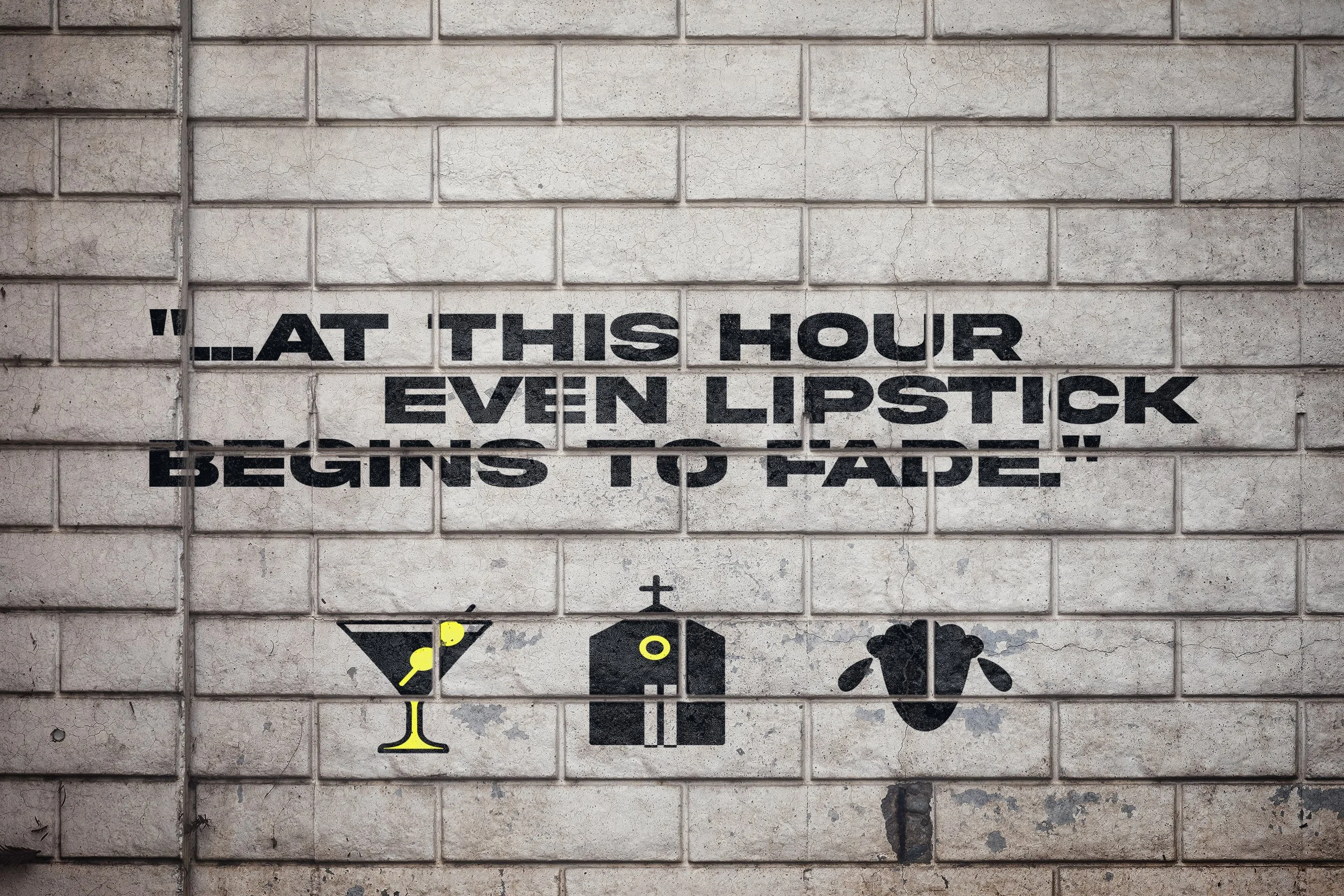 A section of a brick wall with a quote painted on it that says, "...at this hour even lipstick begins to fade". Below the quote, there are three icons representing a martini glass with lemon, a gift box with a ribbon, and a bear head.
