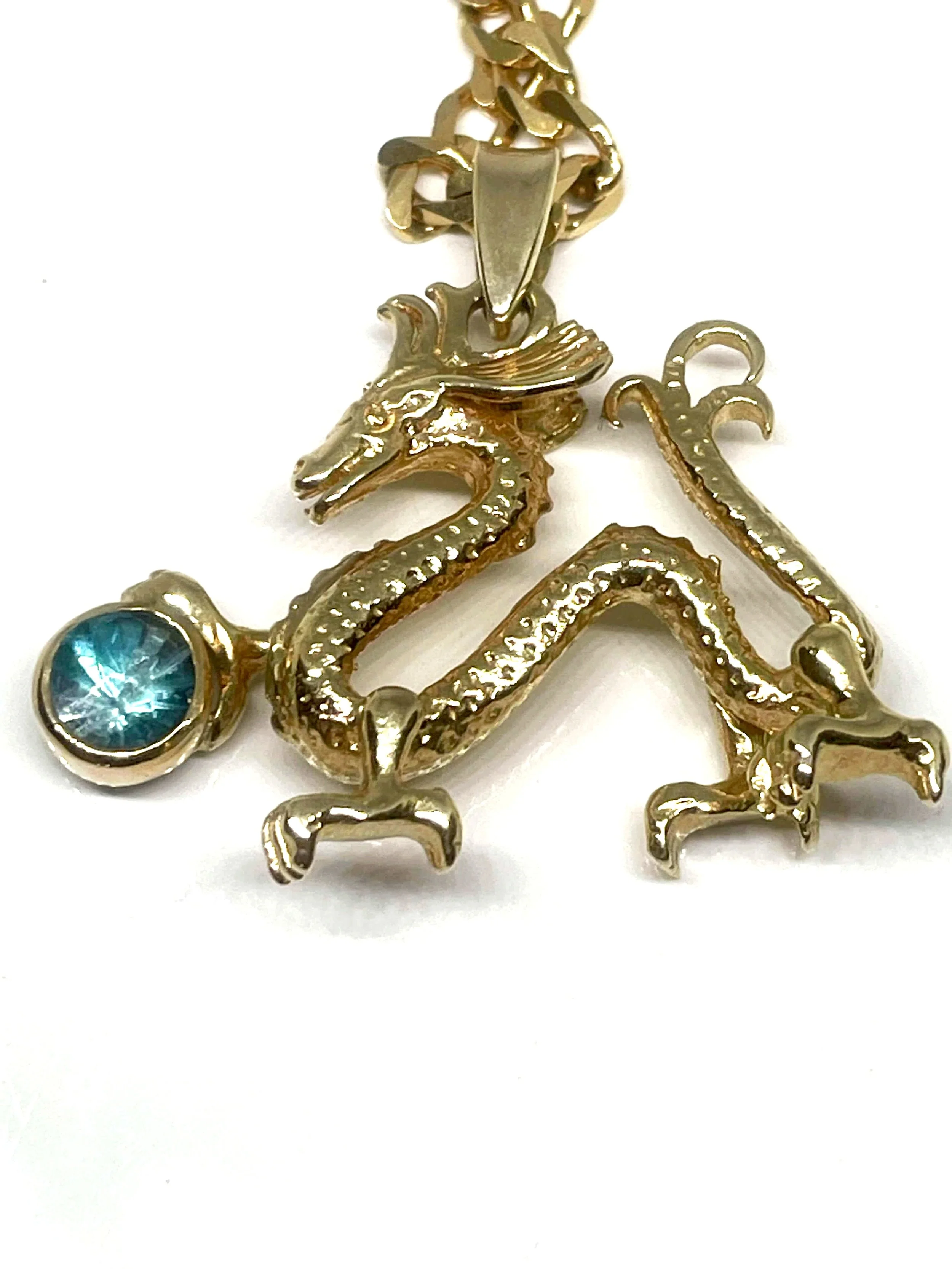 Gold necklace with a dragon pendant, featuring a blue gemstone at the dragon's tail.