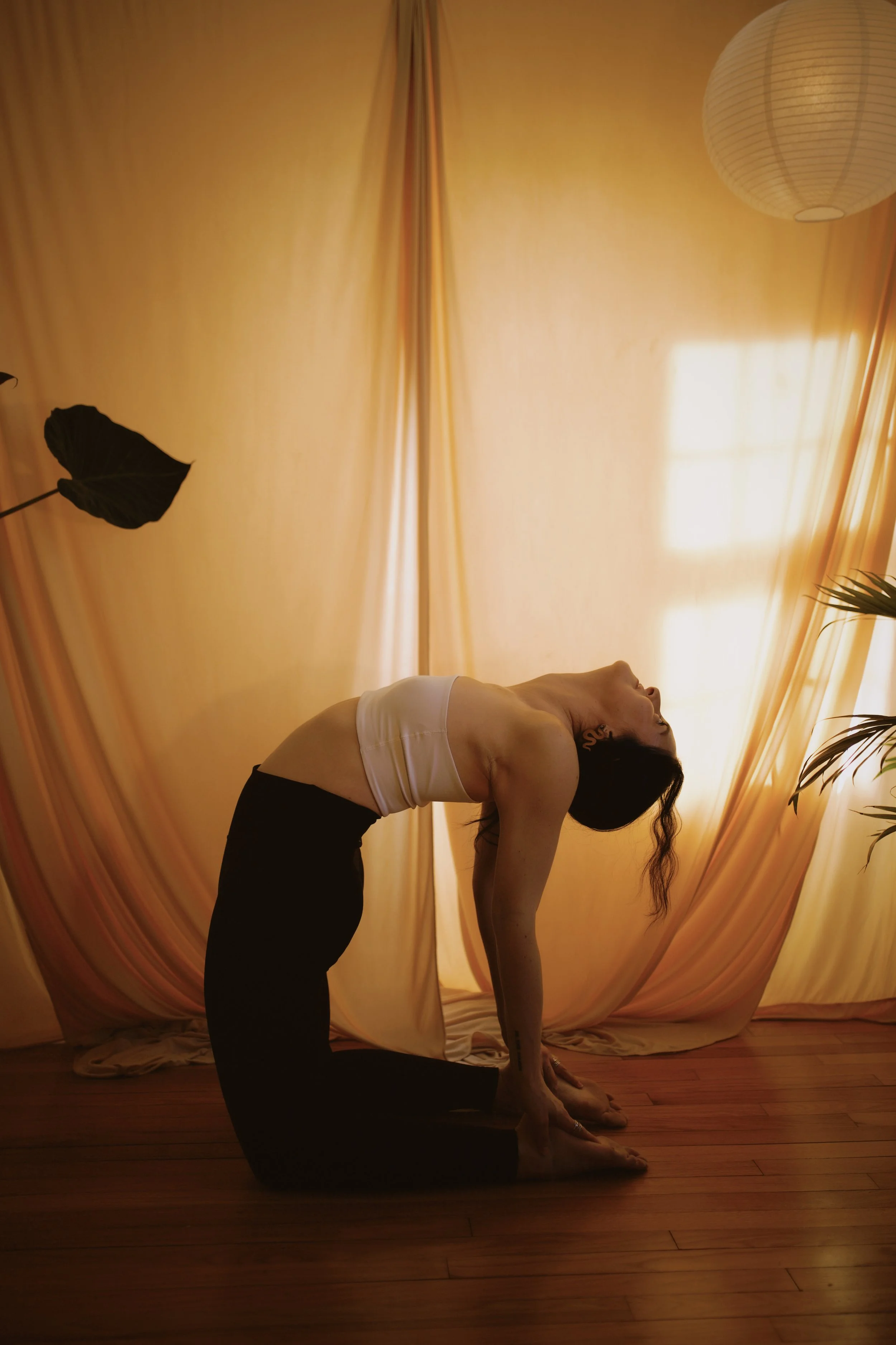 Woman practicing yoga lying on her back on a yoga mat in a room with wooden flooring and plain gray wall