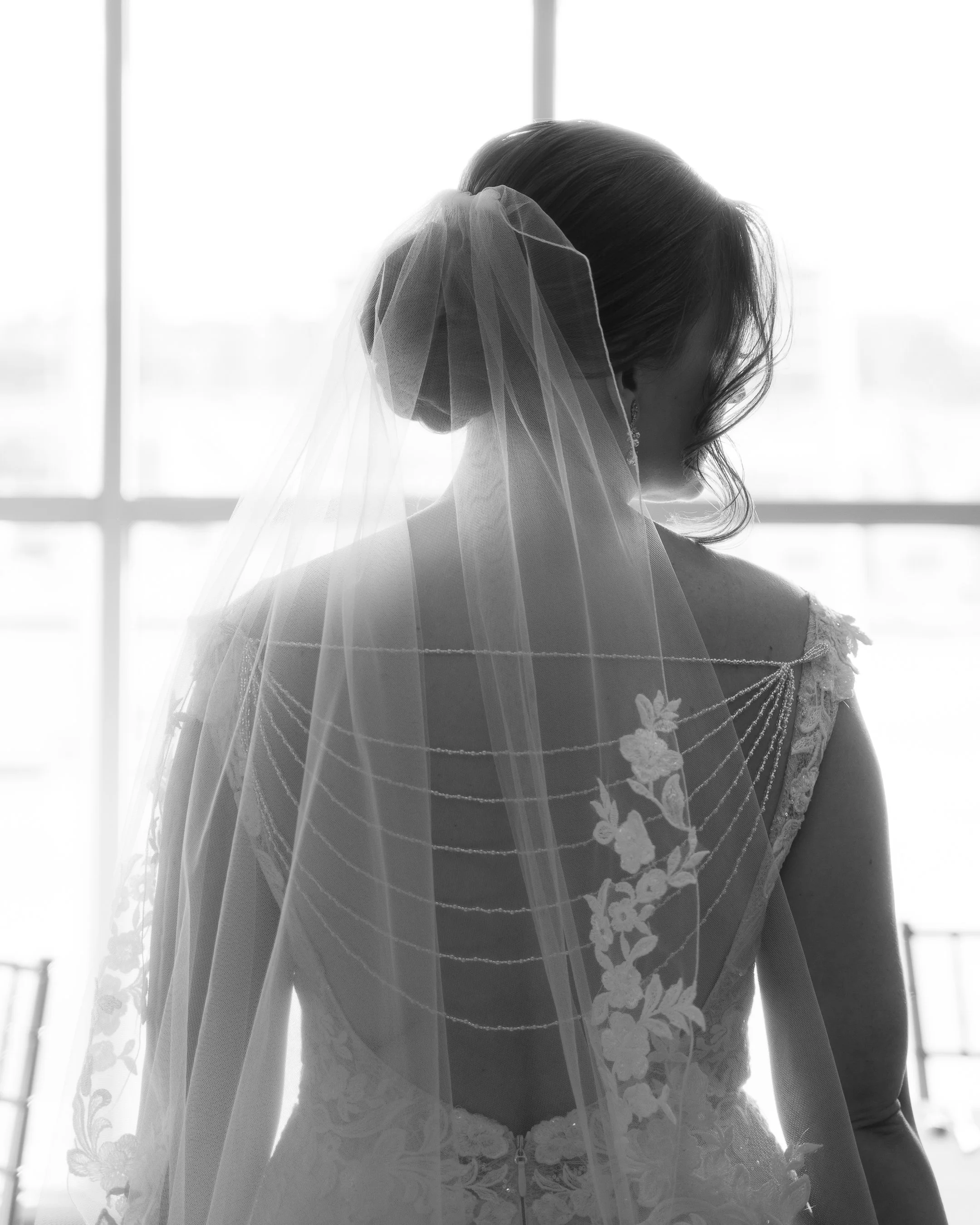 Bride with a wedding veil and lace dress looking out a window