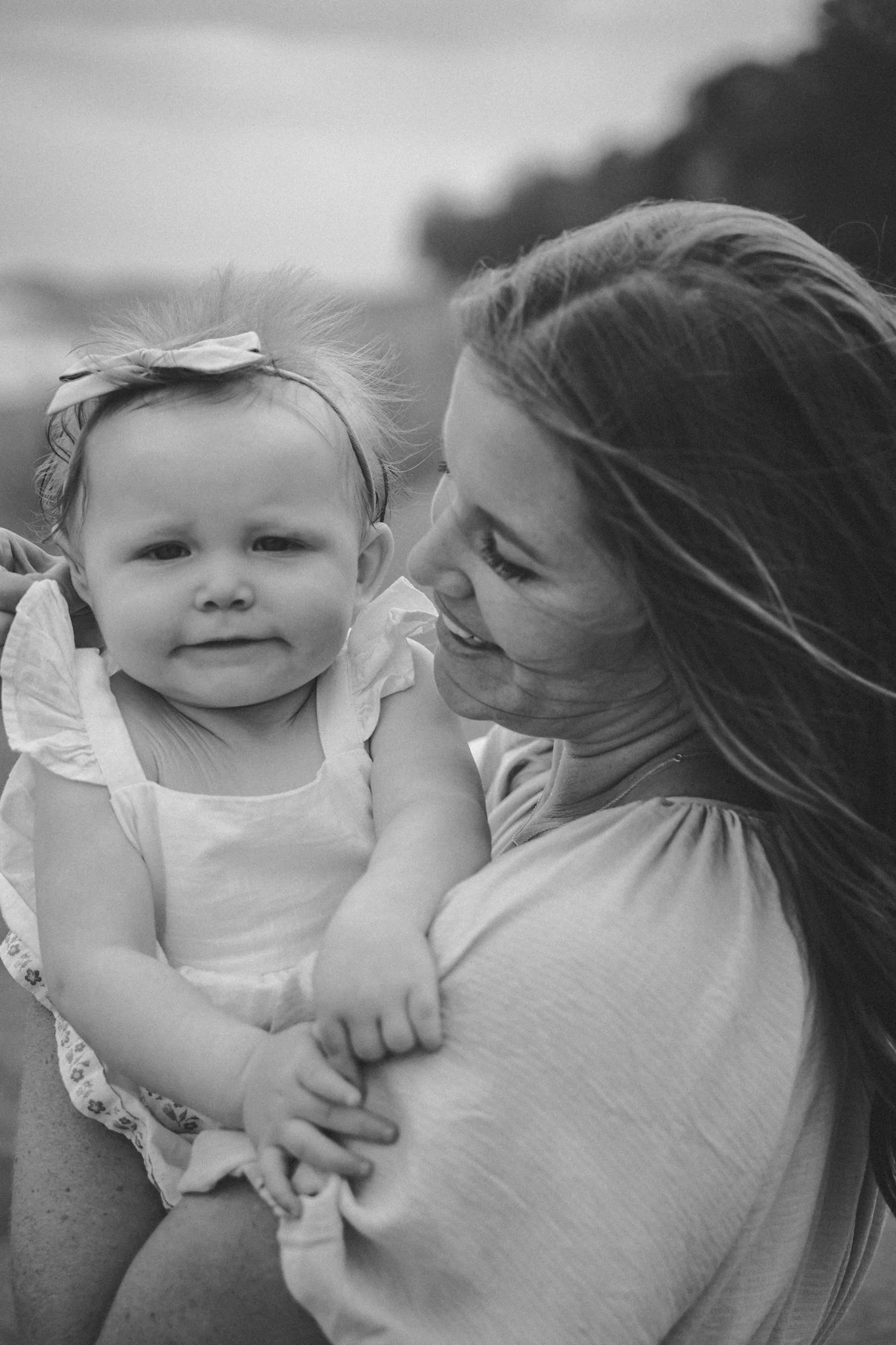 A woman holding a smiling young girl outdoors, black and white photo.