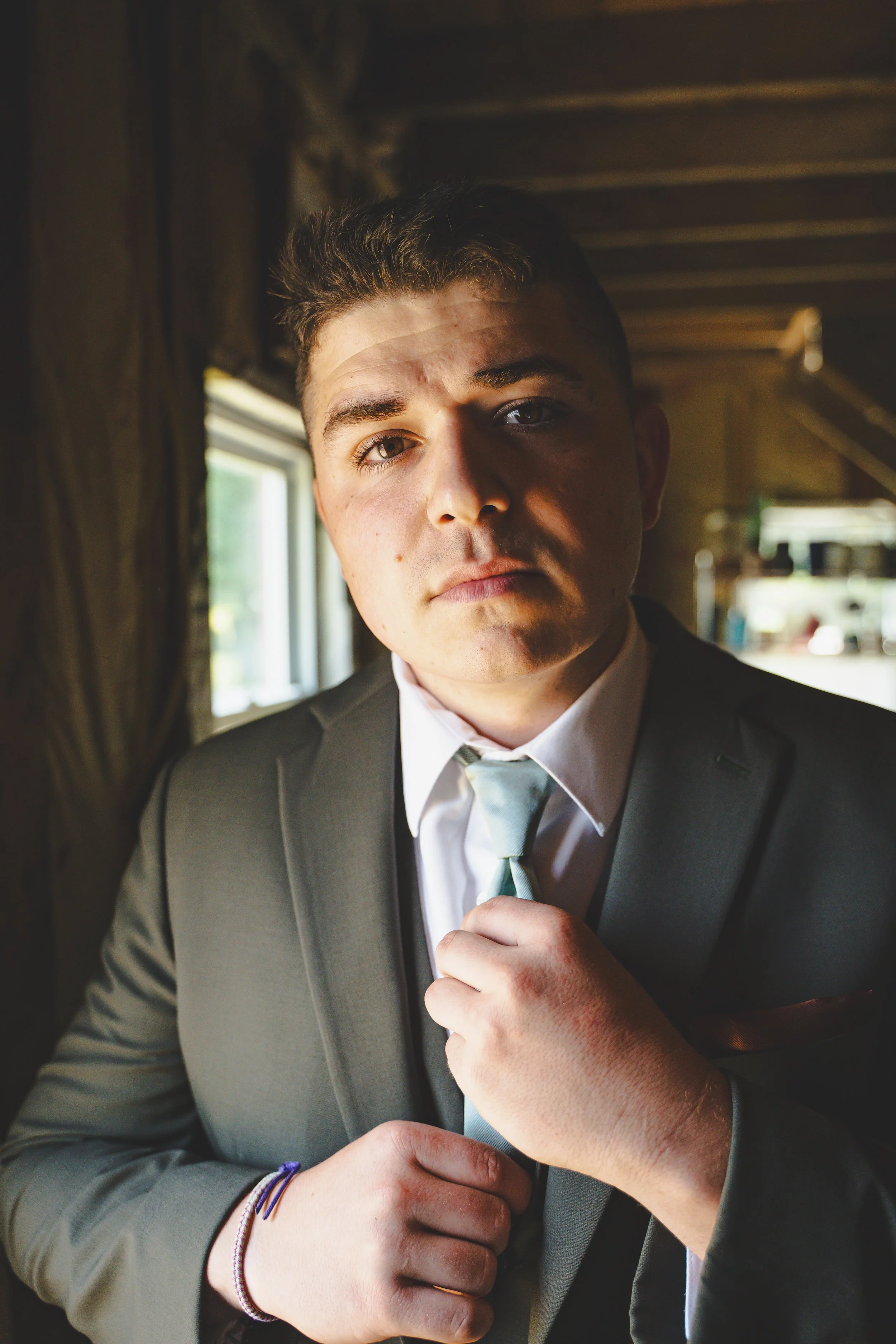 Young man in a suit adjusting his tie indoors near a window.