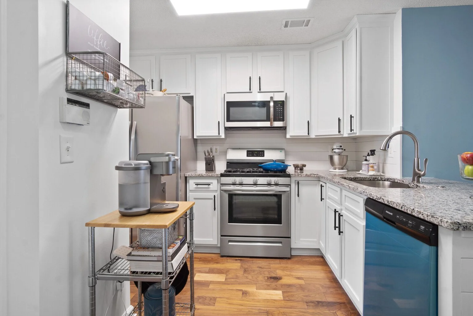 Modern kitchen with white cabinets, stainless steel appliances, granite countertops, and blue accent wall.