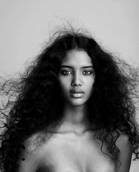 Black and white portrait of a woman with long, curly hair, looking directly at the camera.