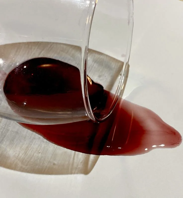 Red wine spilled on a white surface with a glass tilted, causing the wine to spill out.