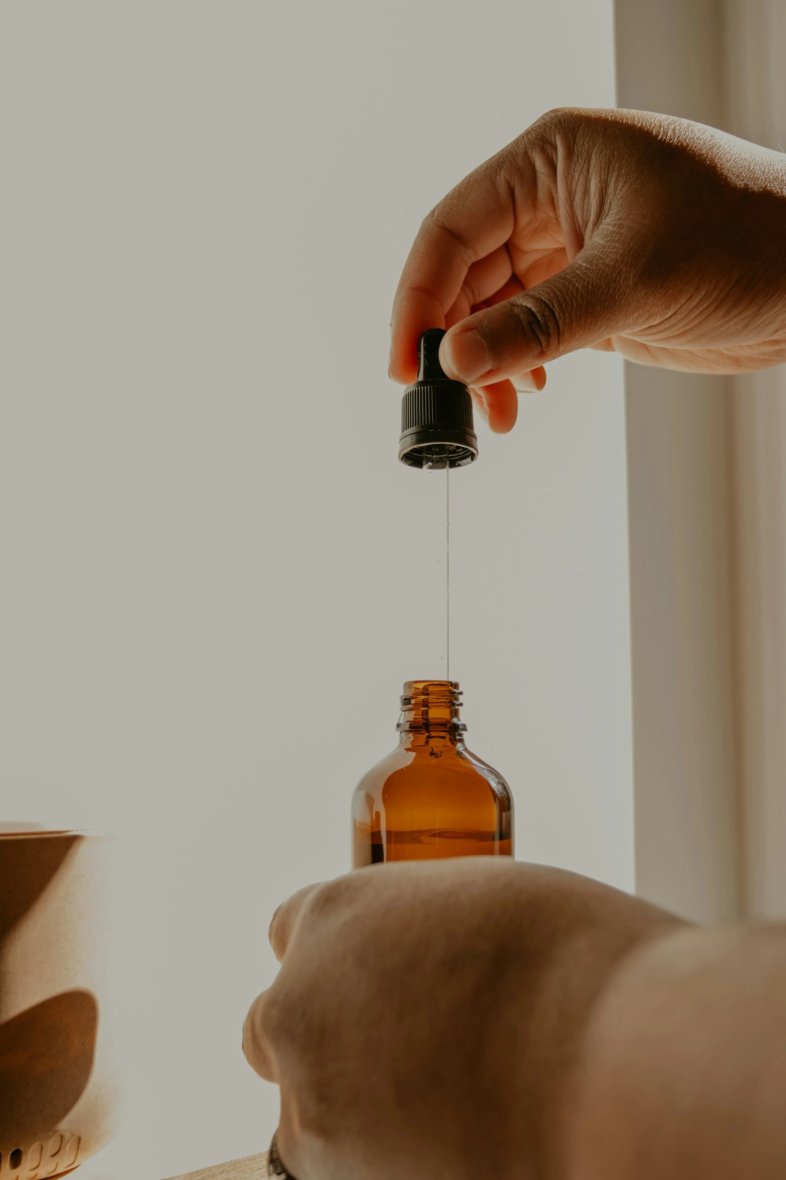 Hand holding a dropper above a brown glass bottle