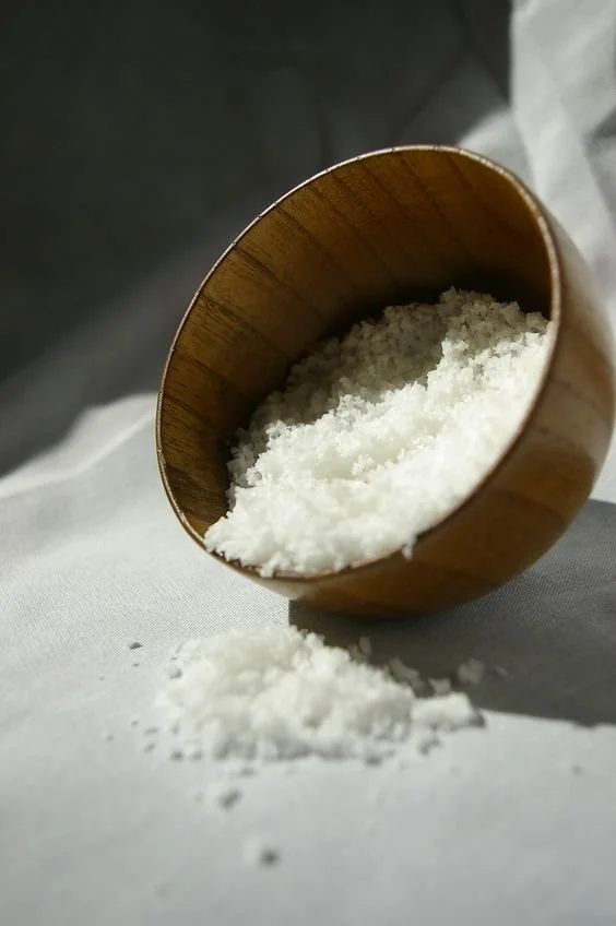 Wooden bowl with coarse sea salt spilling onto a white surface