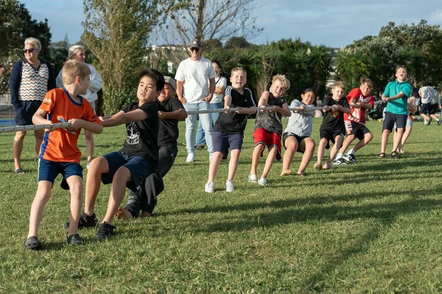 Children and adults playing tug-of-war on a grassy field during daytime.
