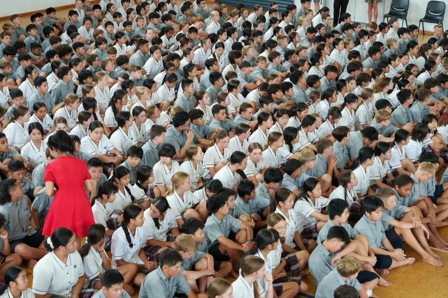 Large group of students sitting on the floor in a school assembly or event.