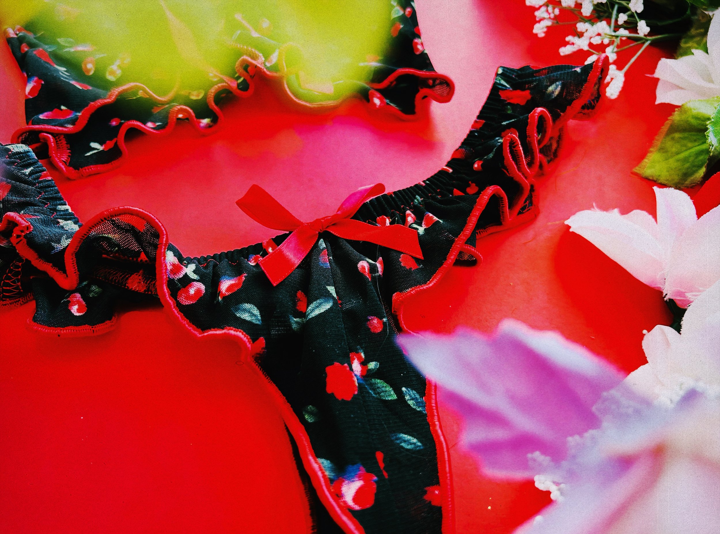 Detailed view of the red ribbon bow on the black floral lingerie, surrounded b soft blurred floral accents for a romantic aesthetic.