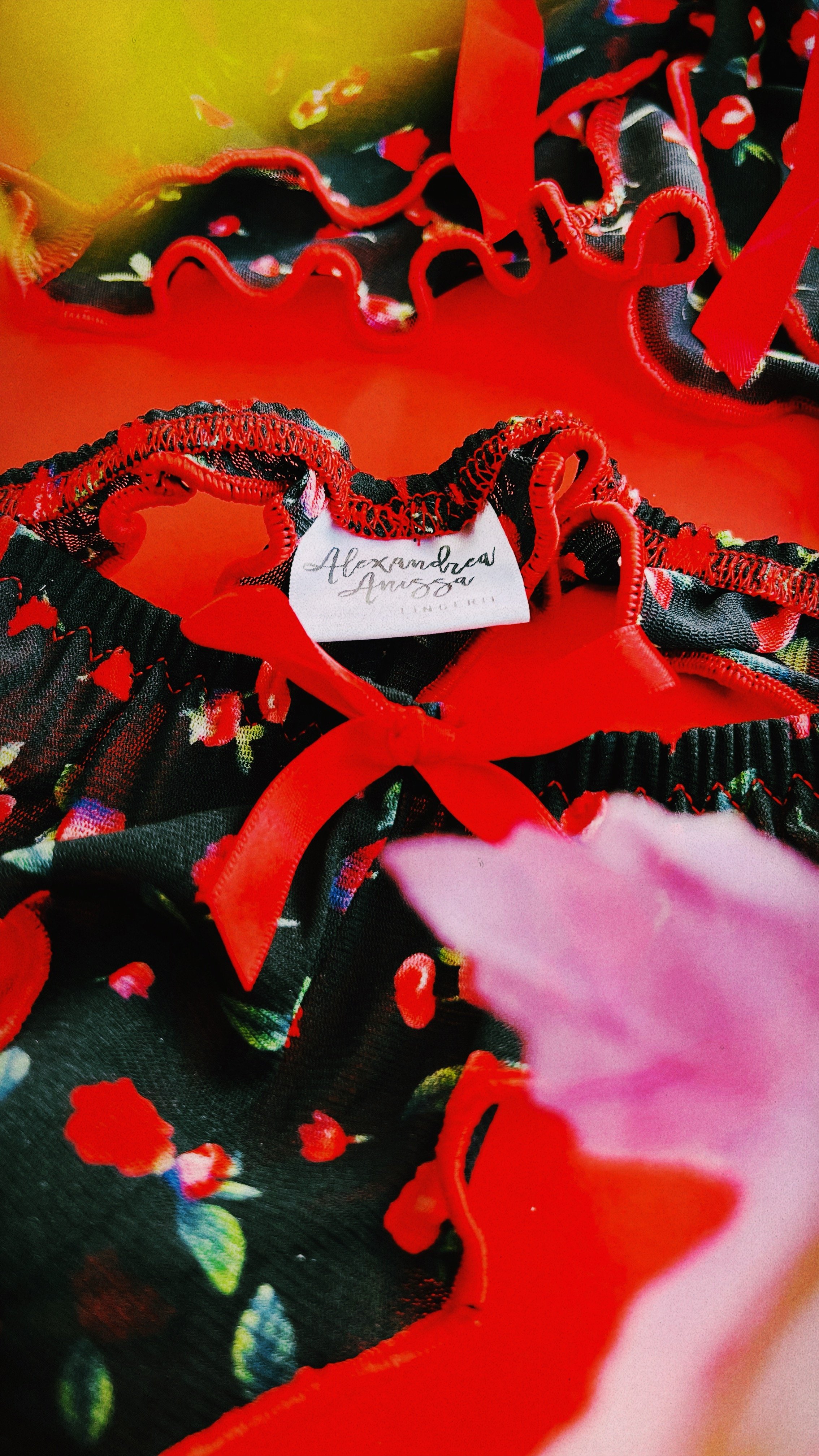 A flat lay of the floral lingerie set with a standout red bow detail, displayed against a vibrant red and floral~themed background.