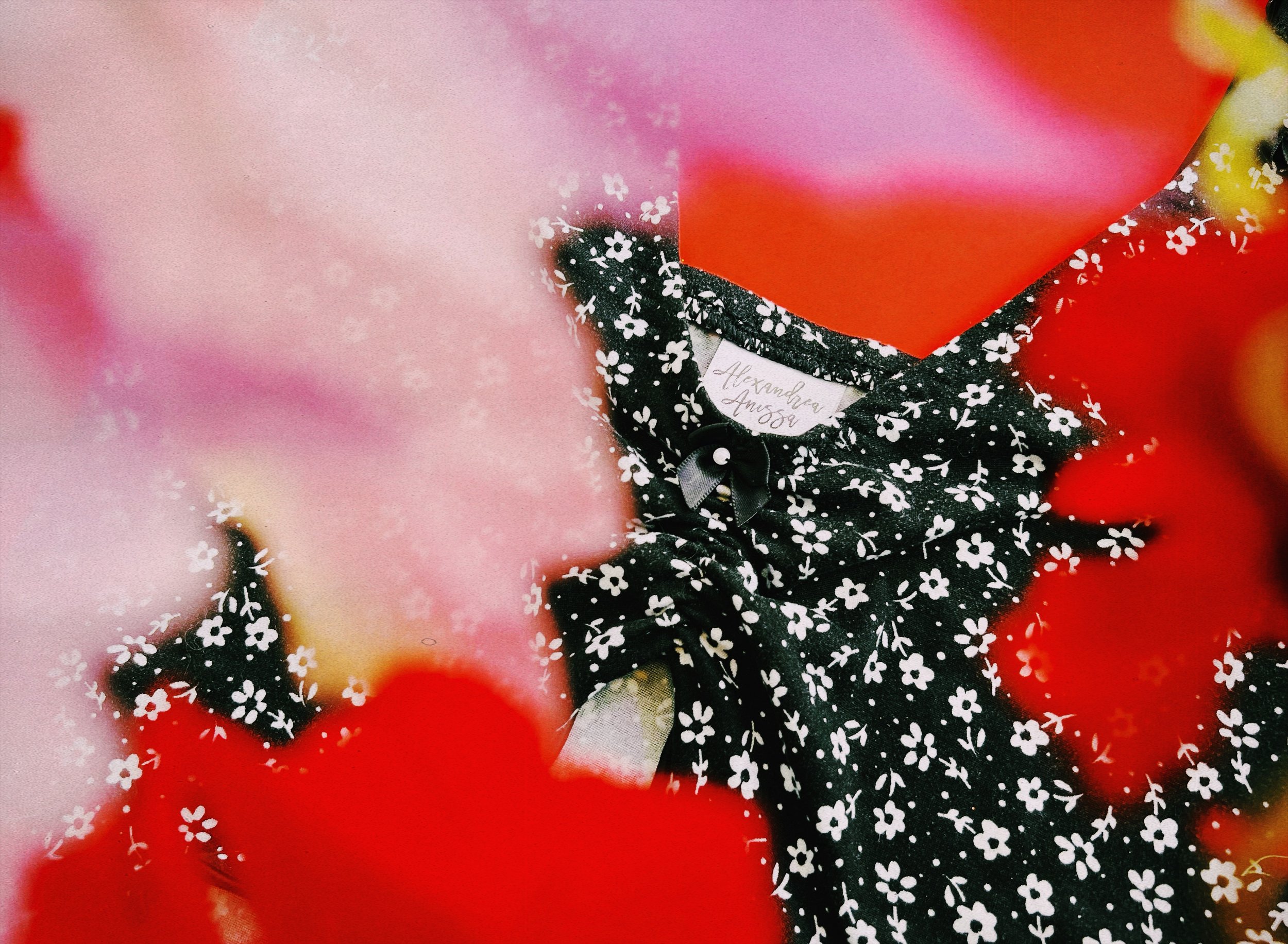 Black cami top with white floral print displayed on a flat surface surrounded by red and pink floral arrangements for a romantic look.