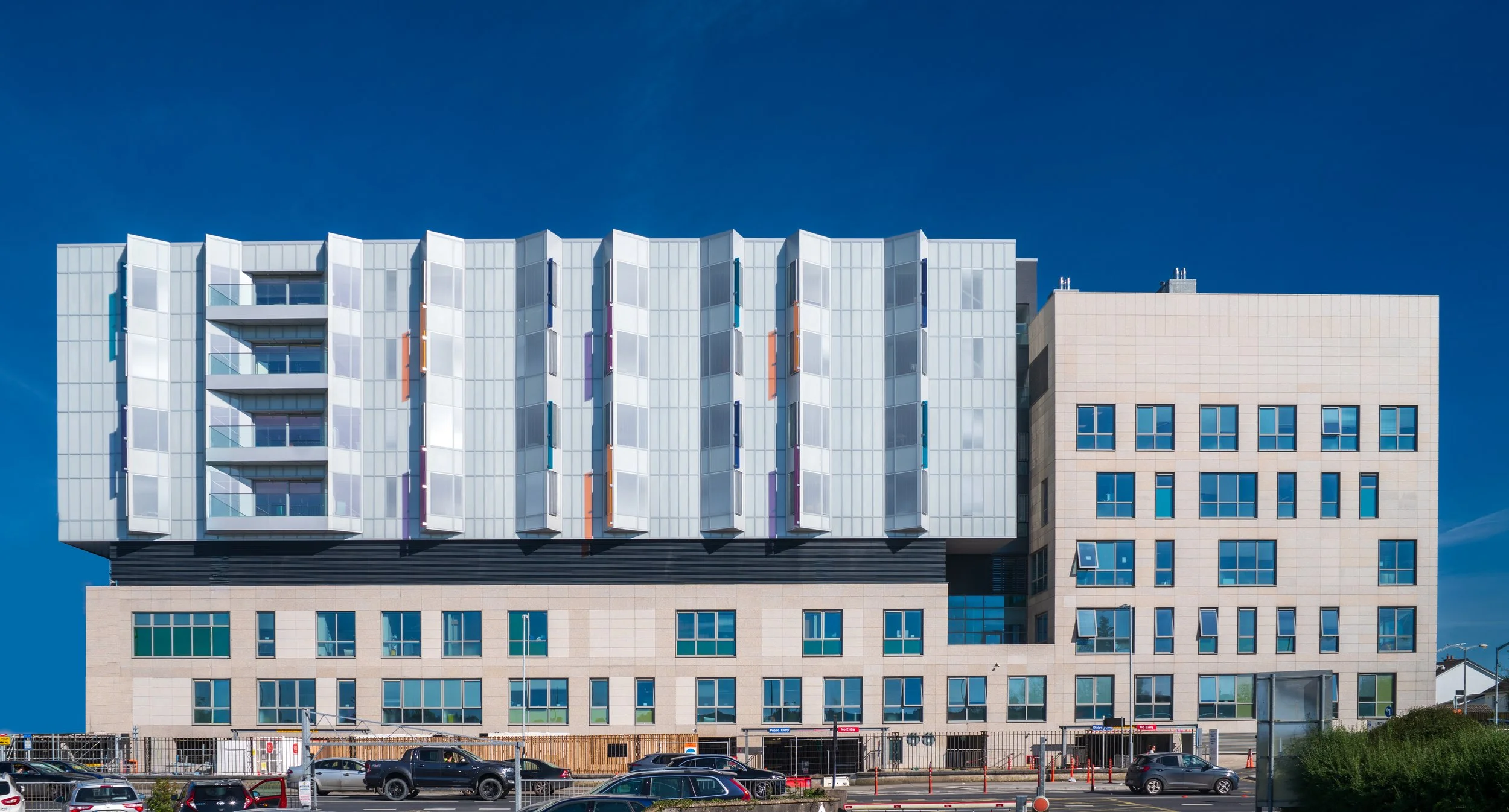 Modern multi-story building with a distinctive white and colorful facade and multiple windows, under a clear blue sky.