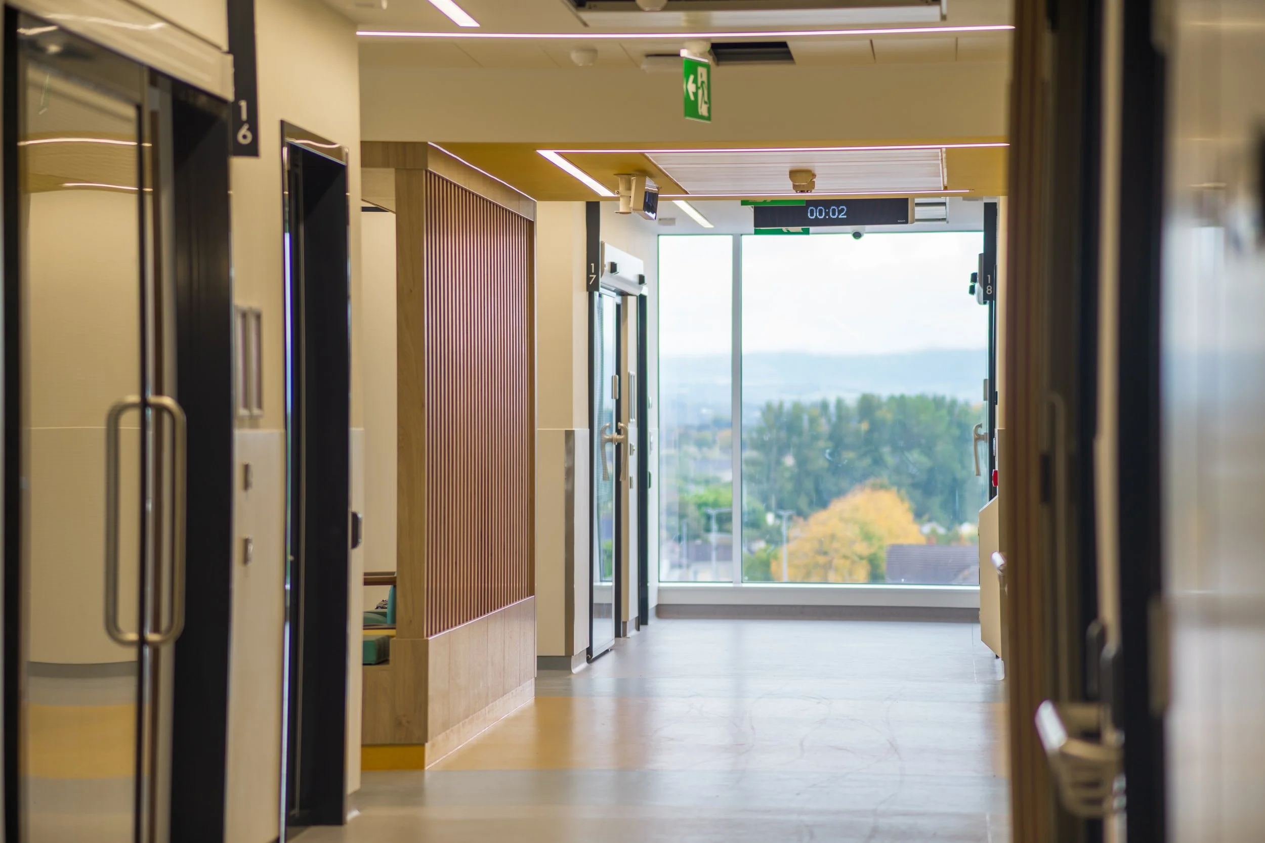 Empty hallway in a modern building with elevators and large window at the end showing a distant landscape.