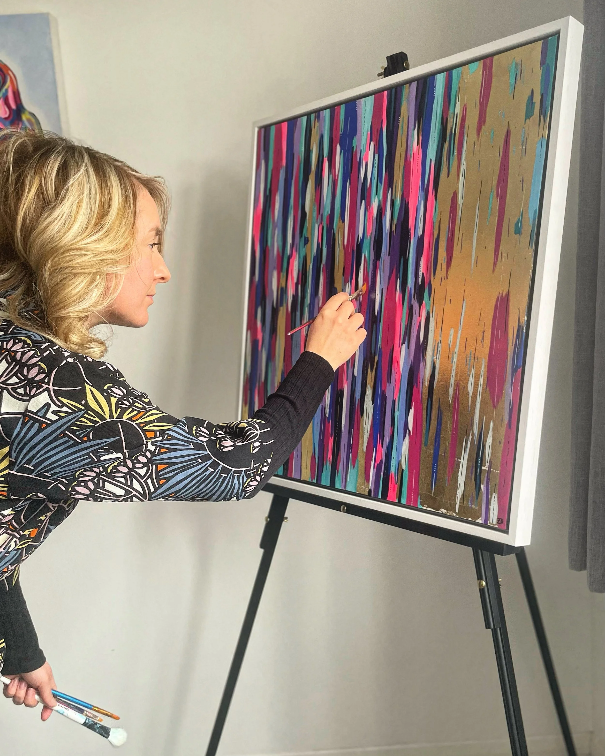 Woman painting an abstract colorful artwork on a large canvas in a studio.