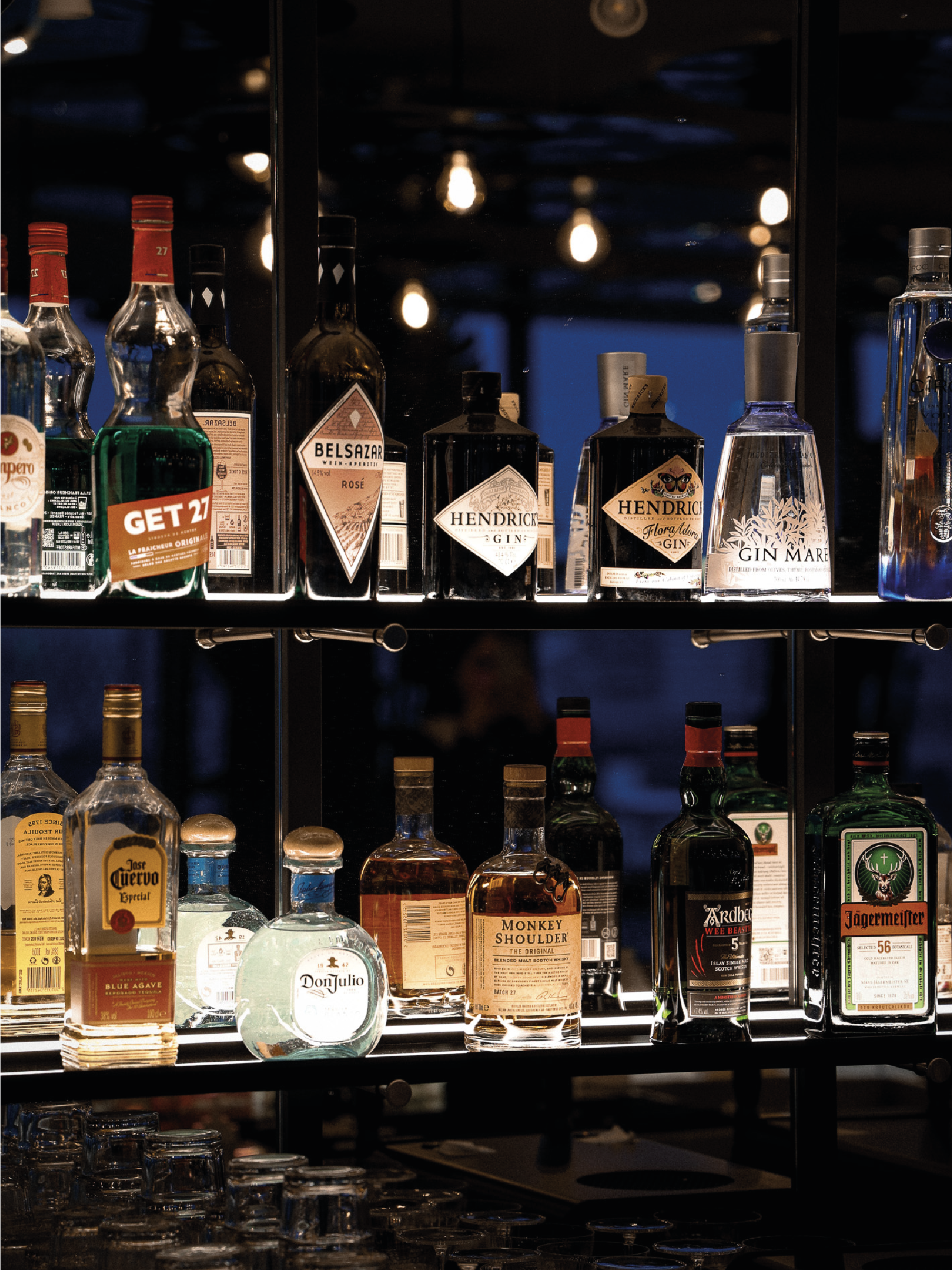 Une étagère de bouteilles d'alcool dans un bar, avec des lumières suspendues au plafond en arrière-plan.