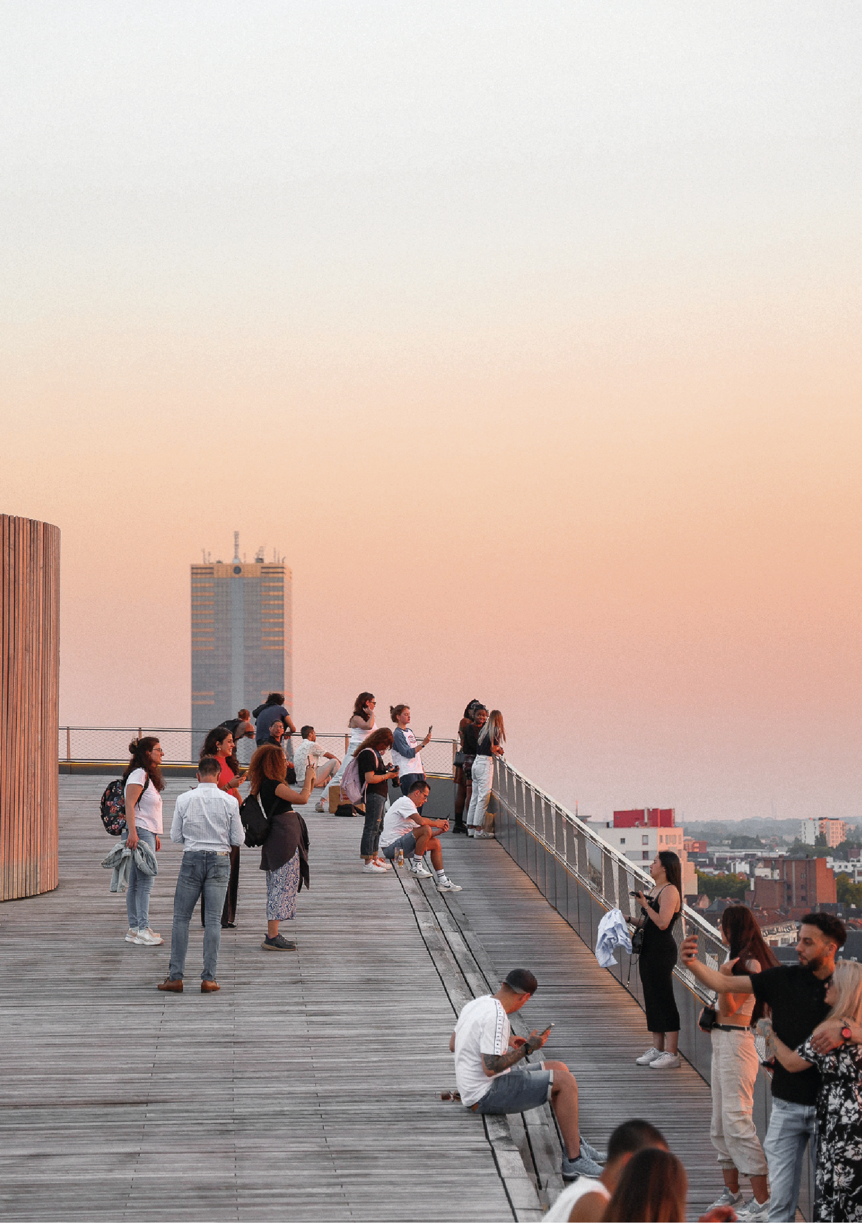 Groupe de personnes sur une terrasse au coucher du soleil, certaines regardant en horizon, d'autres utilisant leur téléphone.