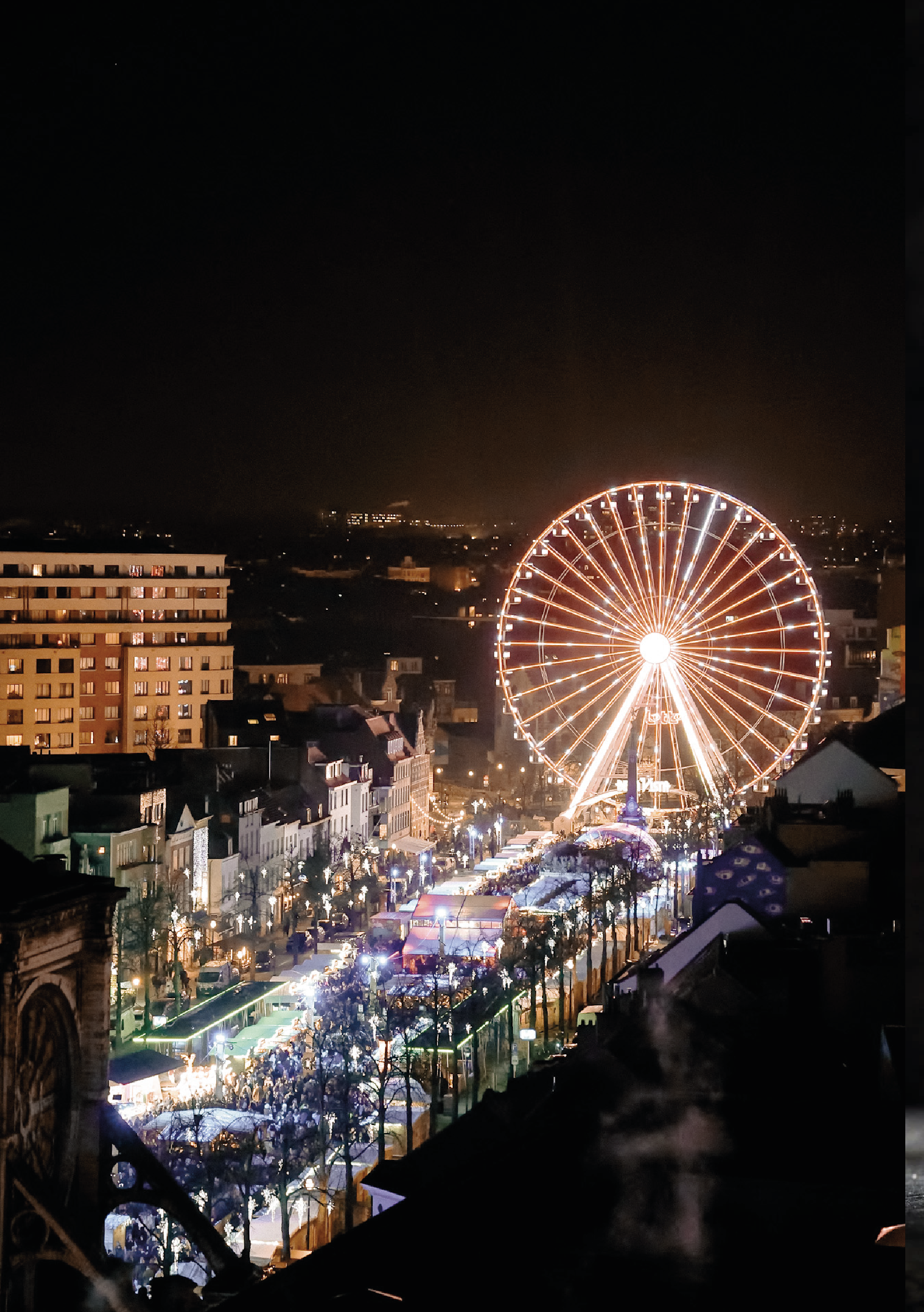 Une grande roue illuminée en fête de nuit, sur une rue animée avec des stands et des lumières, dans une ville animée.