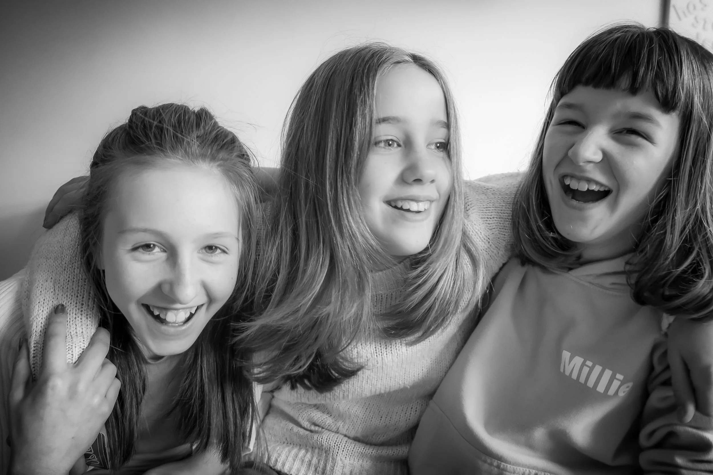 Four young girls with joyful expressions, laughing and smiling, close-up in black and white.