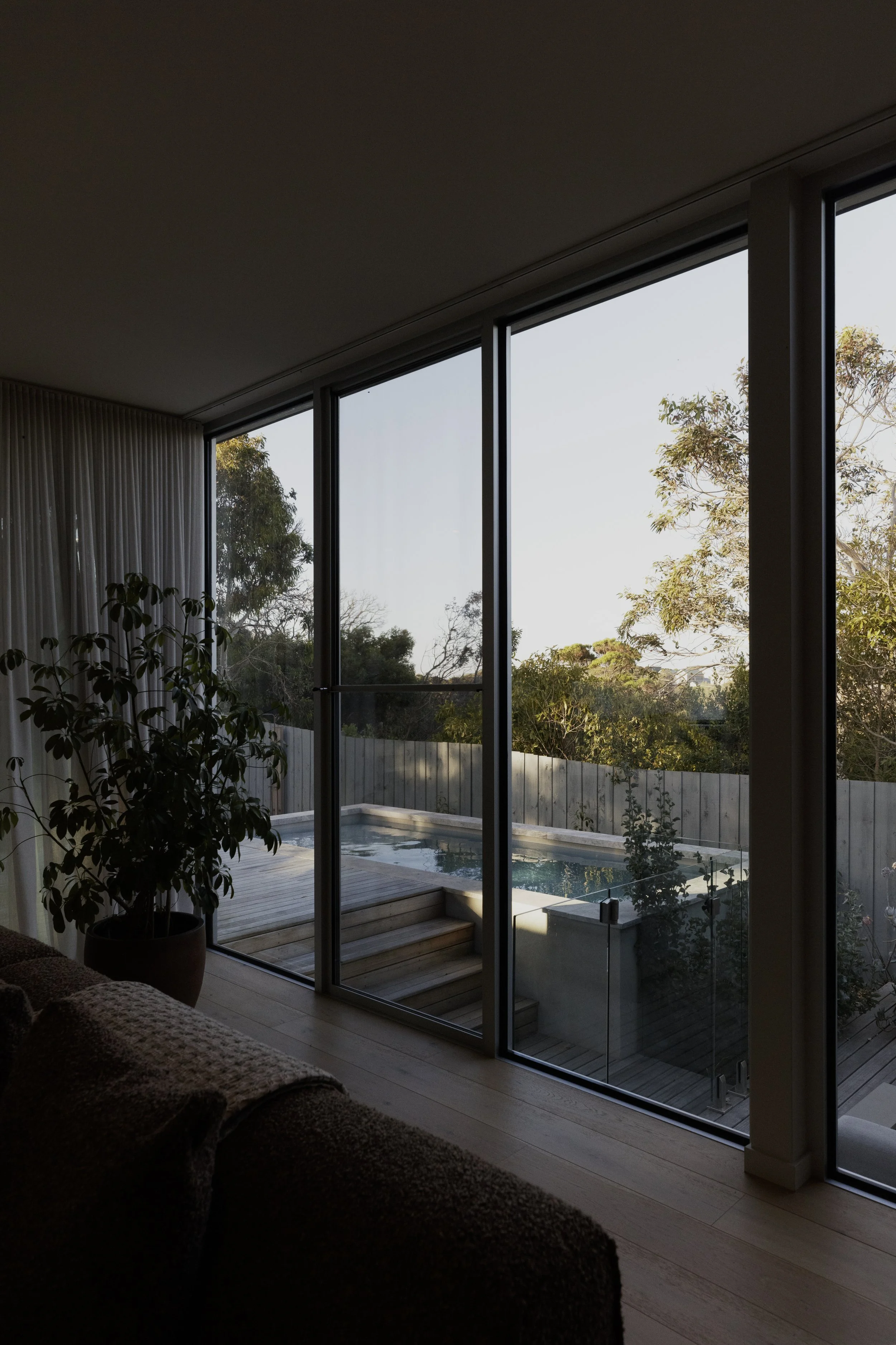 Build by Rawlinson, architecture by Pleaser Perkins. Moody afternoon light through living room windows looking out to a light dappled pool with gumtrees 