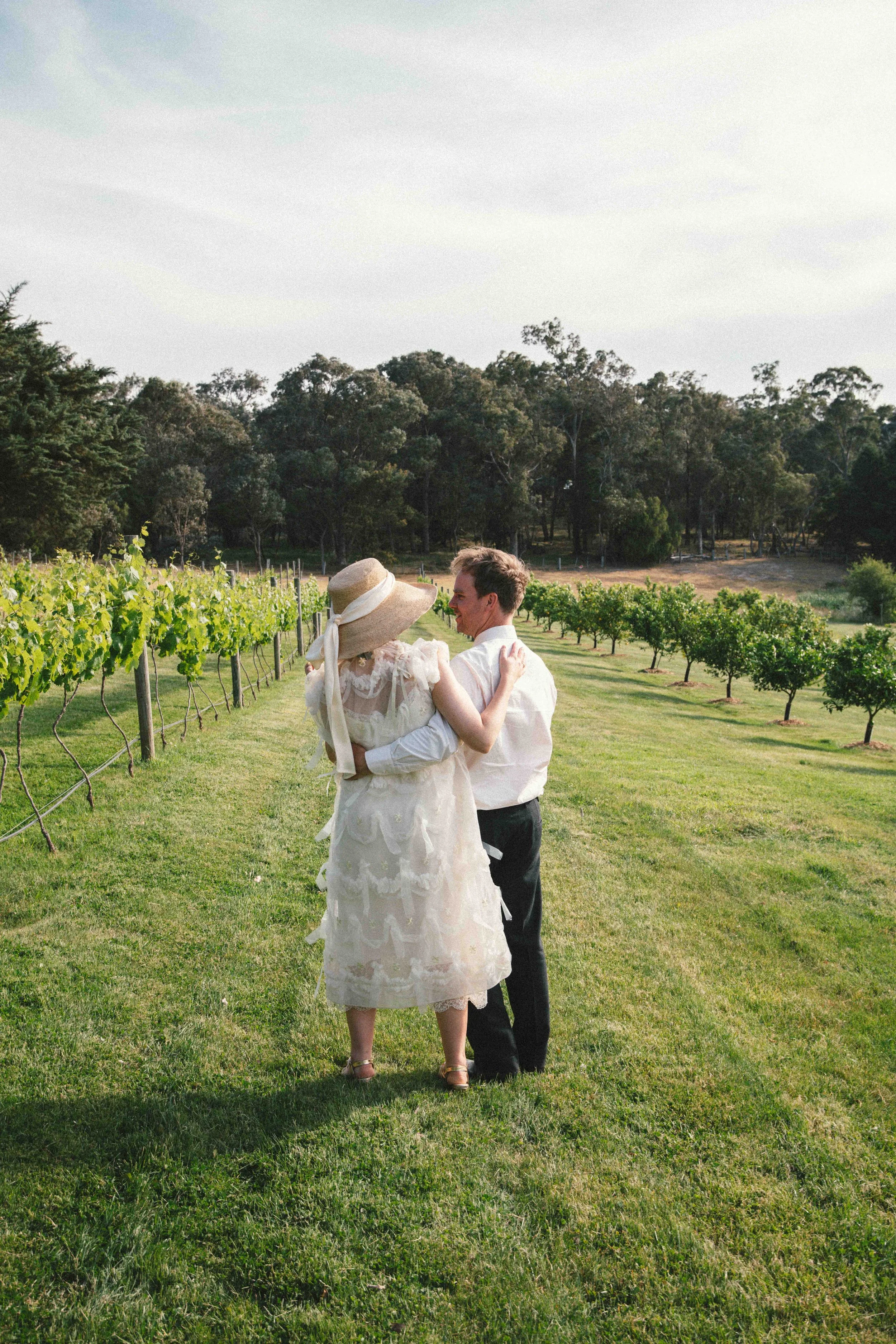 A couple dancing on a grassy field in a vineyard with trees in the background during daytime.