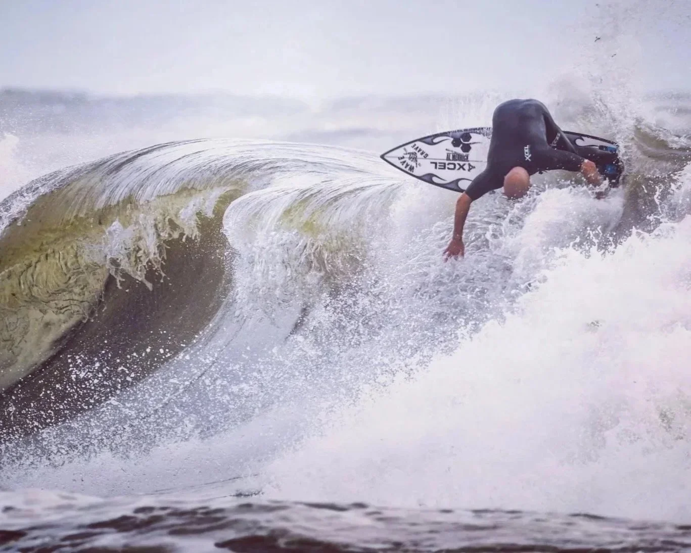 Person surfing on a wave, wearing a black wetsuit and holding a surfboard.