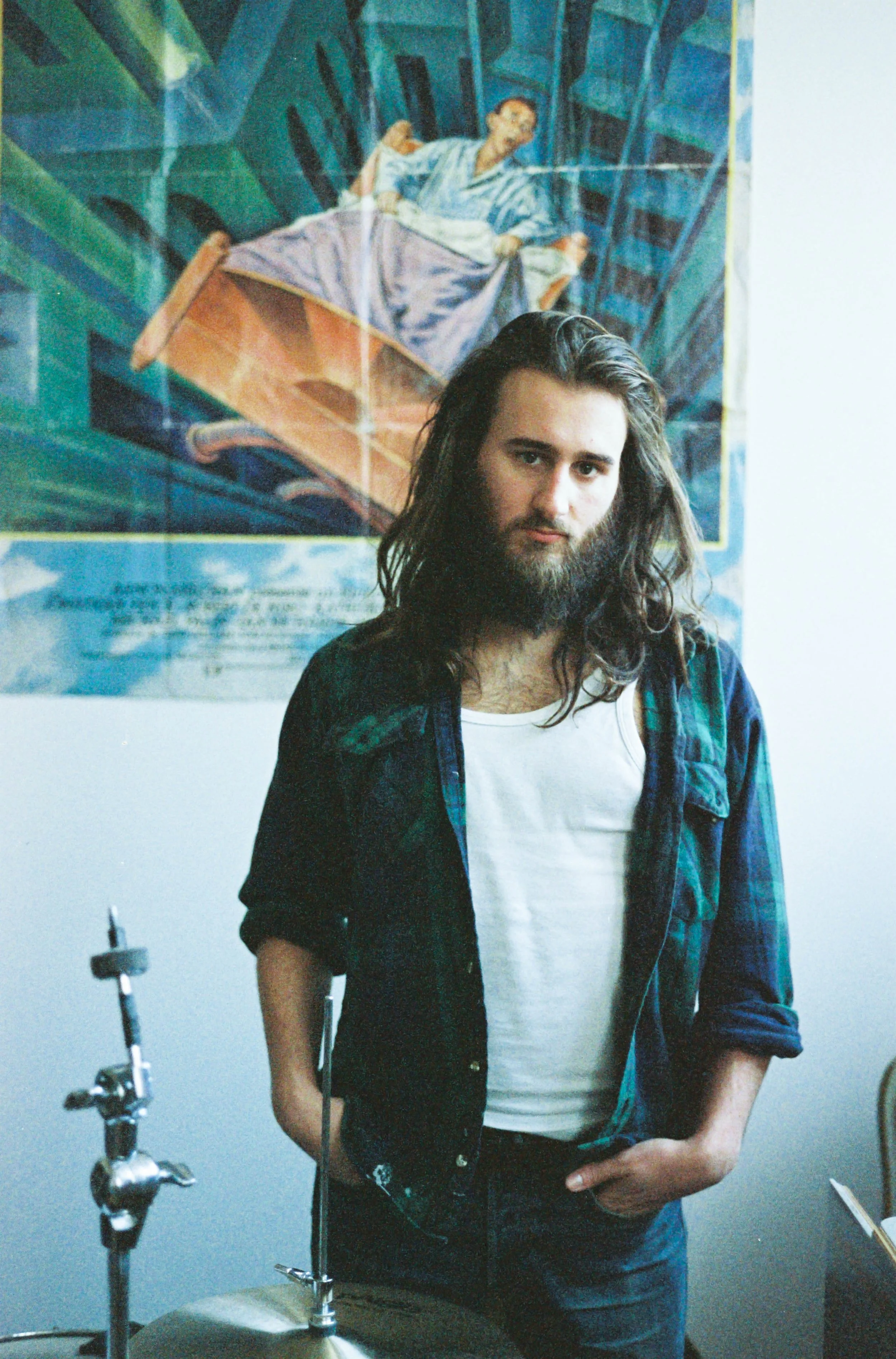 A man with long hair and beard wearing a light denim shirt playing a keyboard.