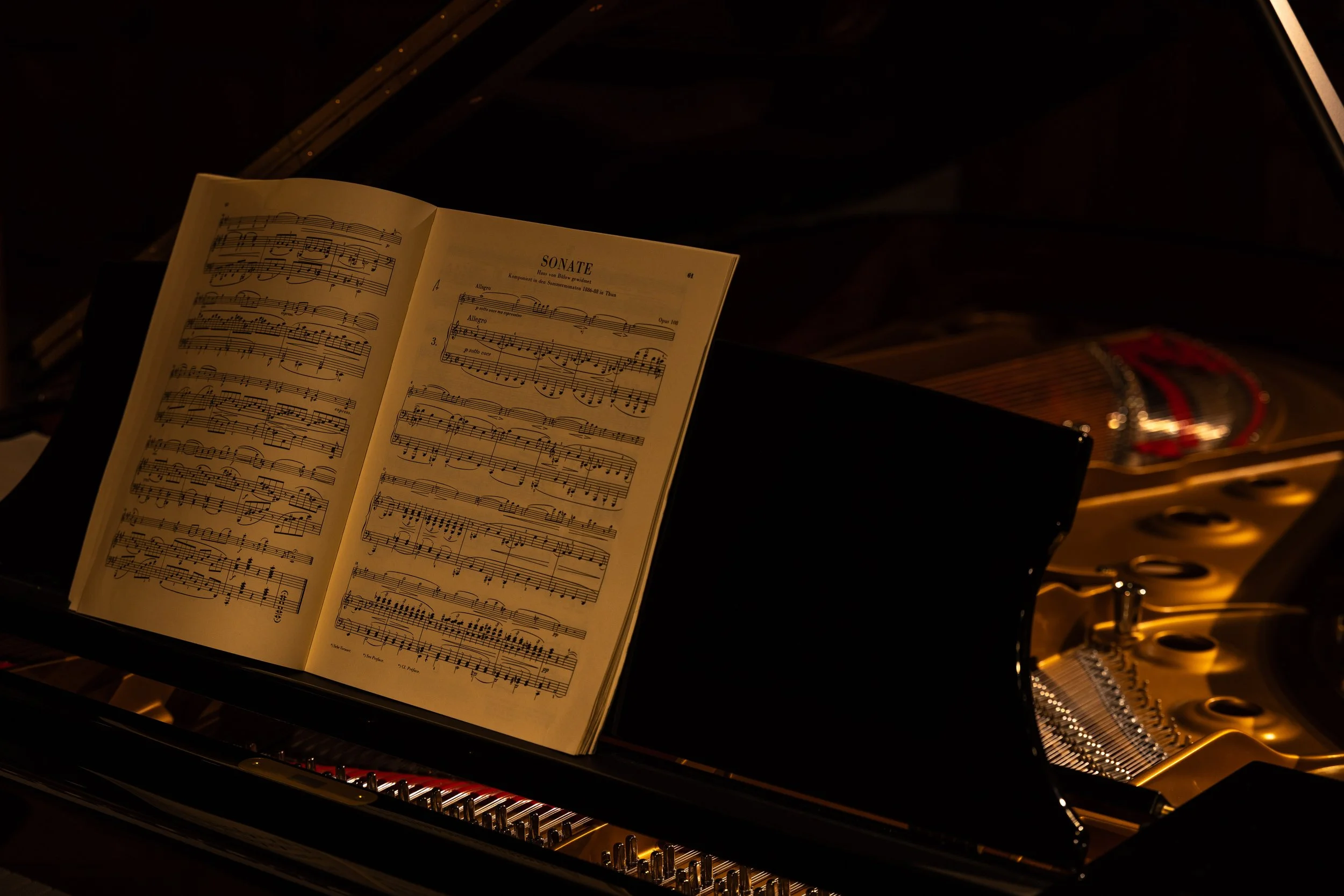 Open music sheet titled 'Sonate' on a grand piano with strings and hammers visible inside, in a dimly lit setting.