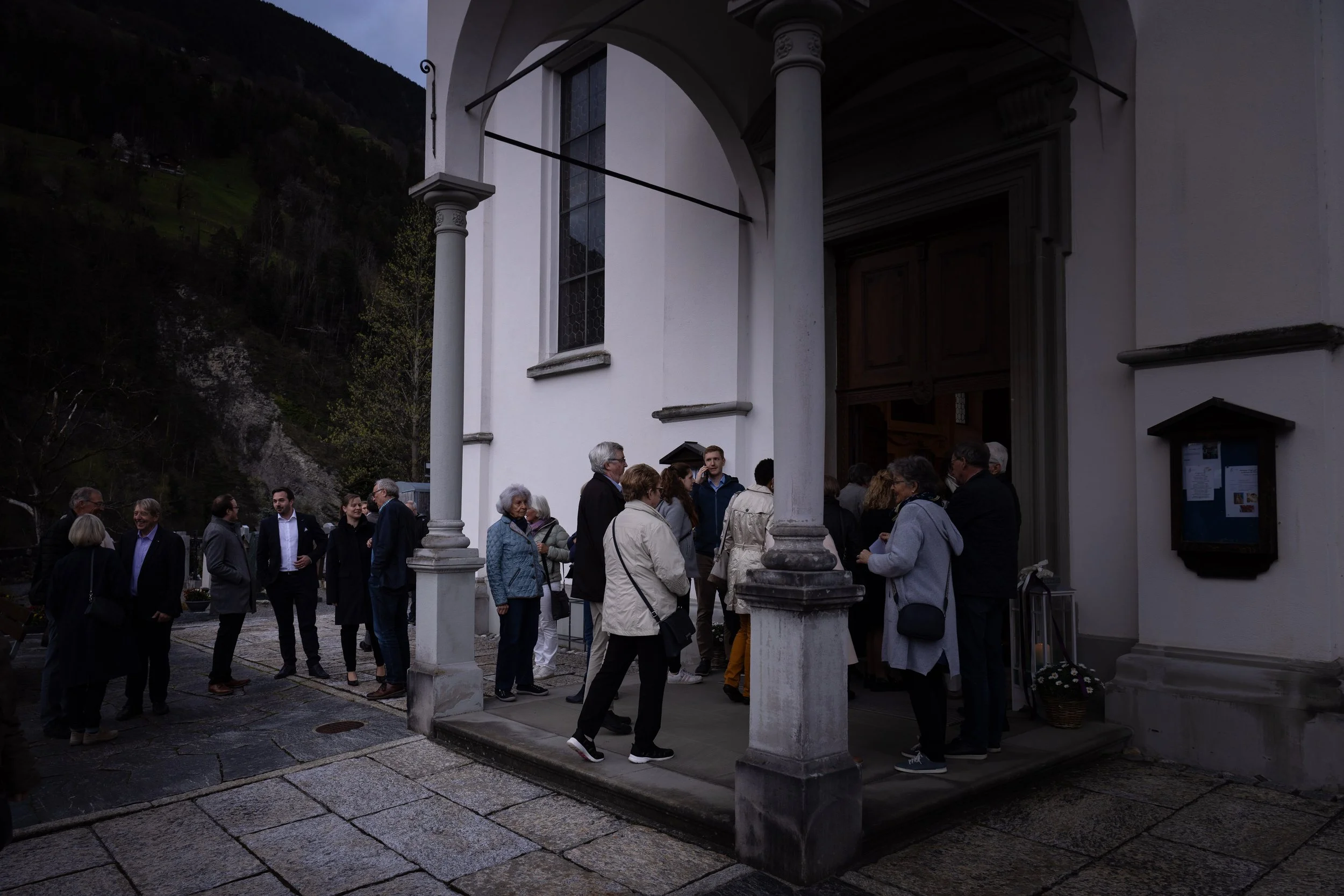 Group of people gathering outside a church entrance in a mountainous area.