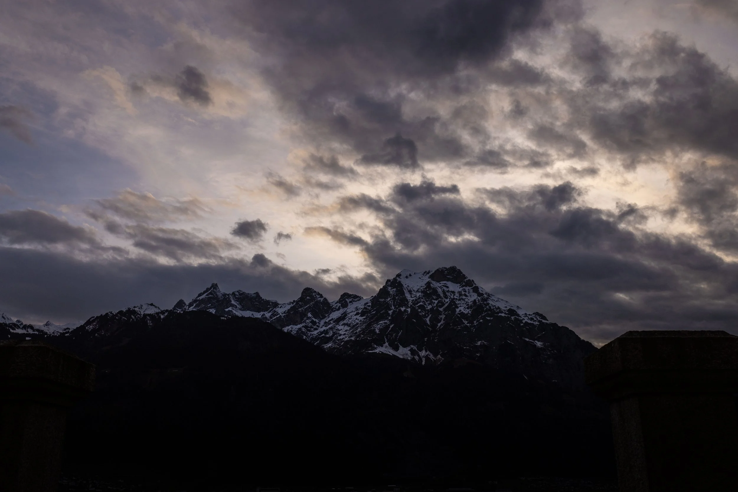 Snow-capped mountains under a dark, cloudy sky during dusk or dawn.