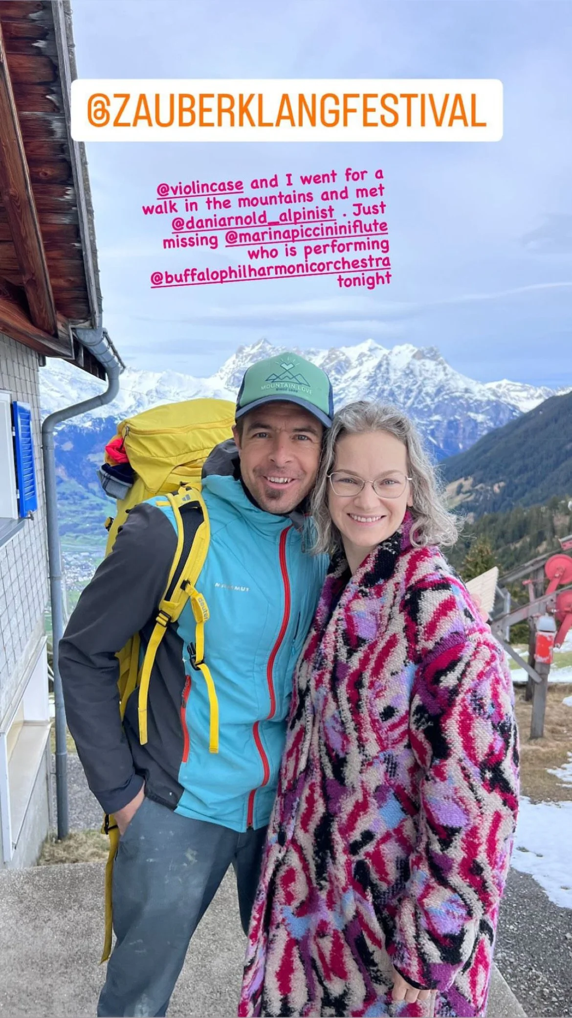 Photo of a man and woman outdoors with snow-covered mountains in the background. The man is wearing a blue jacket and a cap, and the woman is wearing a colorful, patterned coat. There is text on the image mentioning a festival and social media tags.