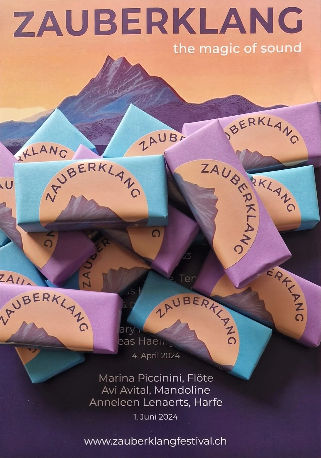 Colorful promotional display for the Zauberklang music festival showing wrapped chocolates and a mountain illustration, with details about the event date, performers, and website.
