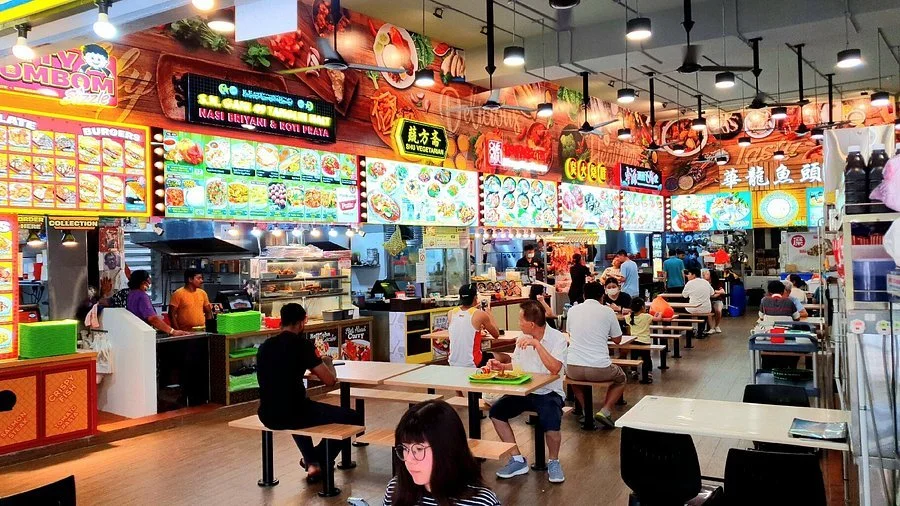 Bustling Singapore hawker center with rows of colorful food stalls and diners eating at communal tables