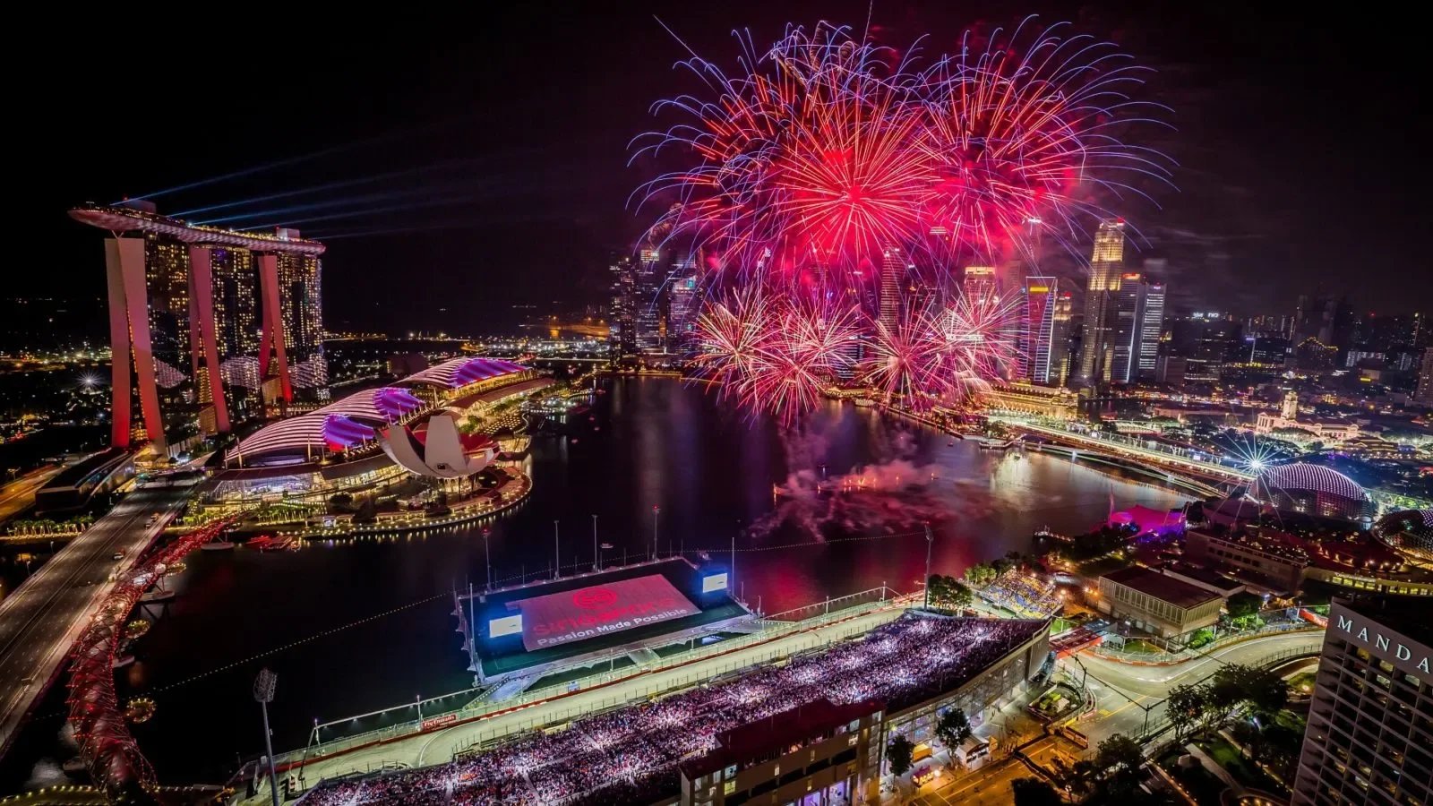 The Marina Bay Street Circuit illuminated under floodlights during the Singapore Grand Prix with the city skyline and Singapore Flyer visible in the background