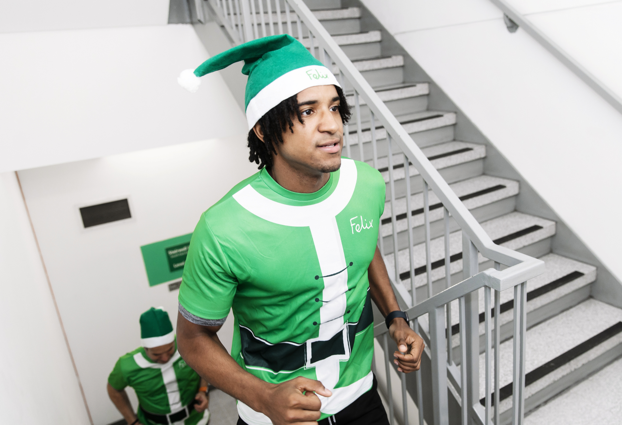 Man climbing the stairs in green santa t-shirt and hat.