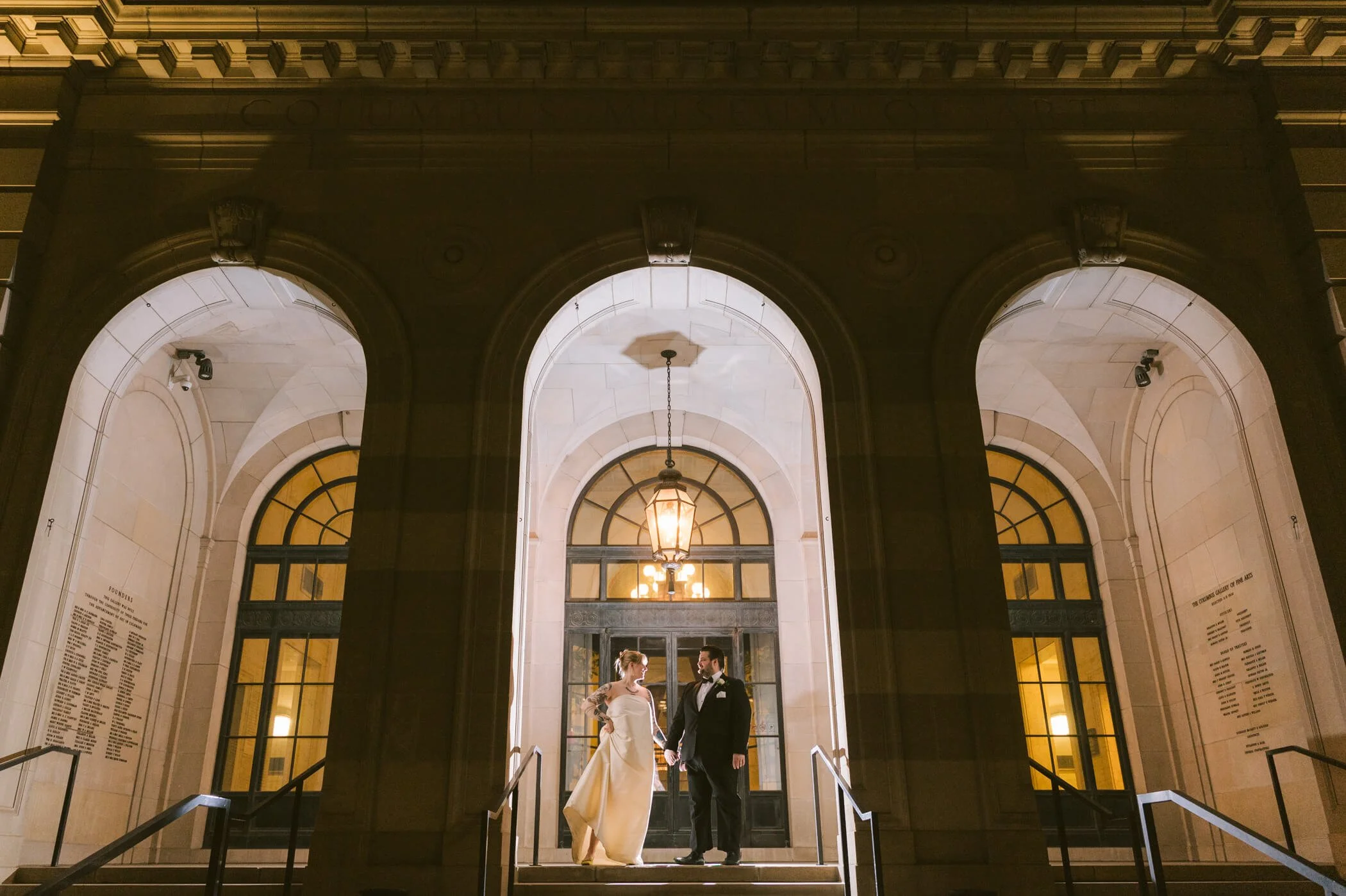 Bride and groom beneath the illuminated stone arches at the Columbus Museum of Art entrance at night