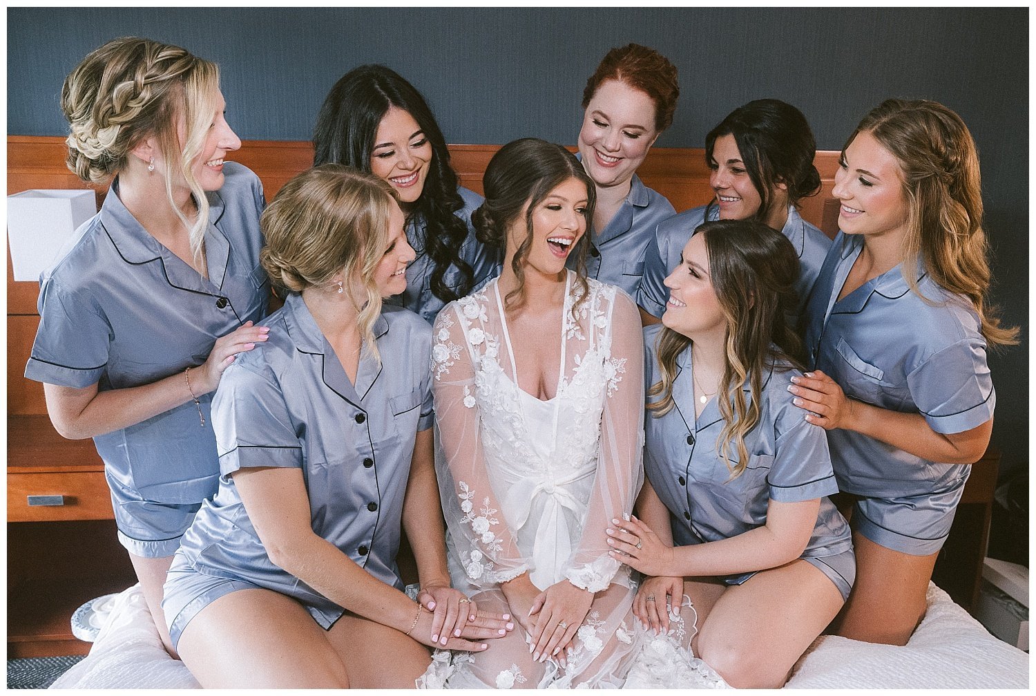 A bride and bridesmaid in matching pajamas on a bed posing for wedding photos