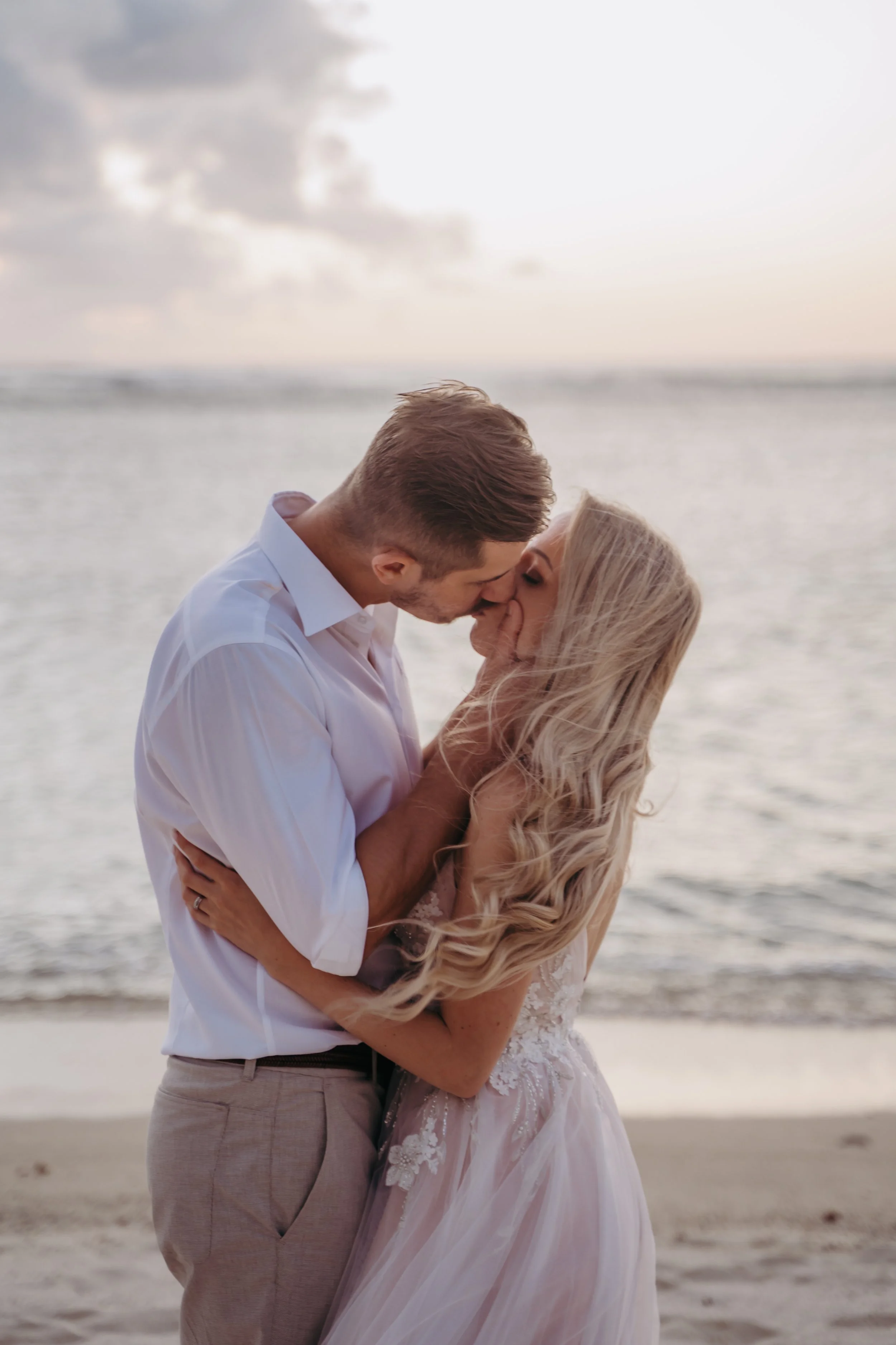 A couple kissing on the beach at sunset, with the ocean in the background.