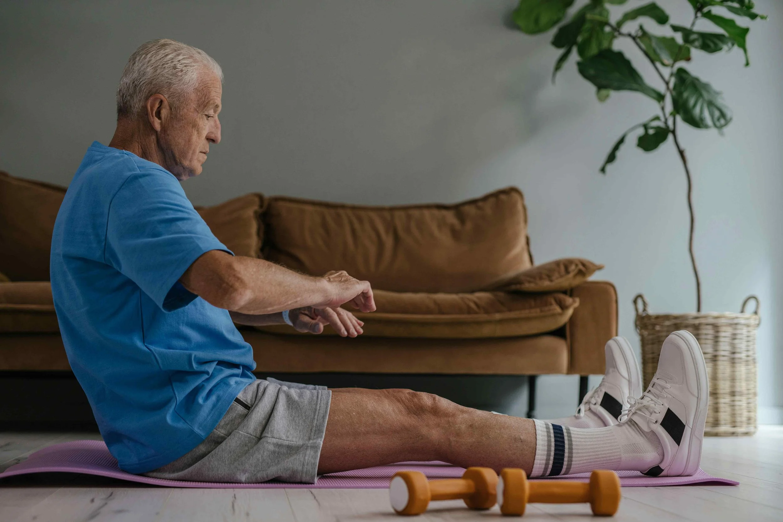 Image of an older gentleman, on the floor, stretching next to weights.