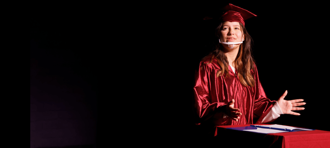 Graduate in red cap and gown speaking at podium on stage